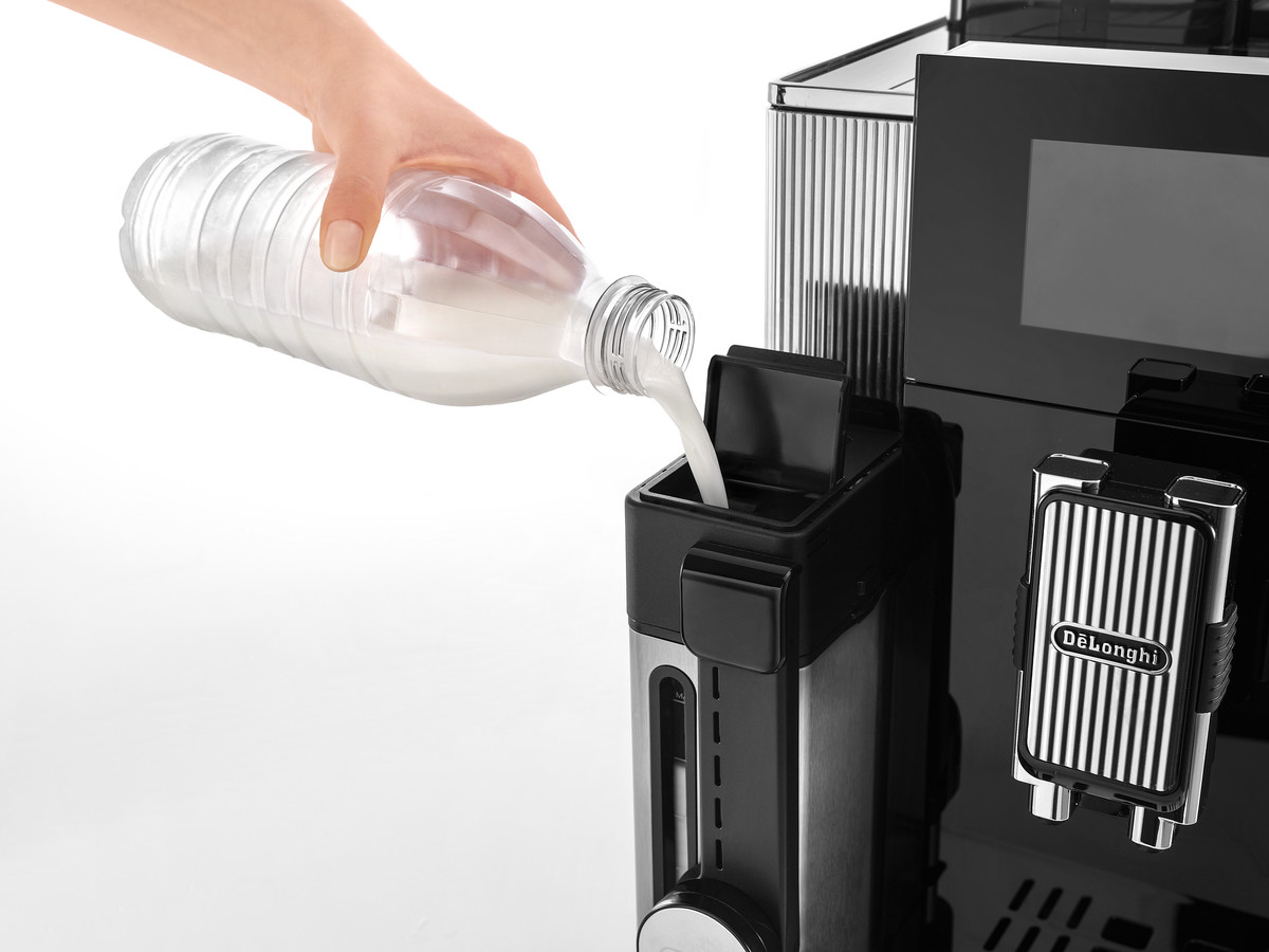 Eine Person gießt Milch aus einer Flasche in den Milchbehälter einer schwarzen Kaffeemaschine.