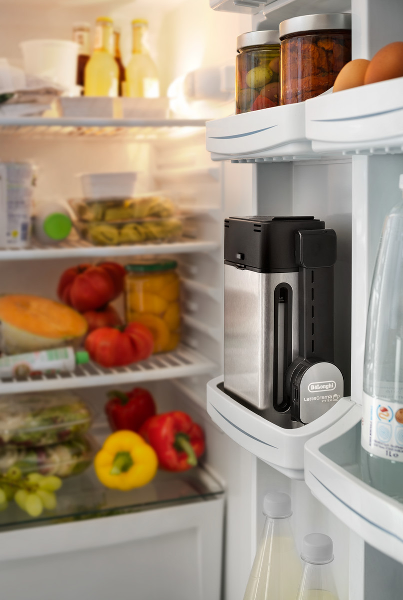 In einem Kühlschrank. Ein Kochgerät steht auf einem Regal, umgeben von Lebensmitteln wie Tomaten und Gläsern.