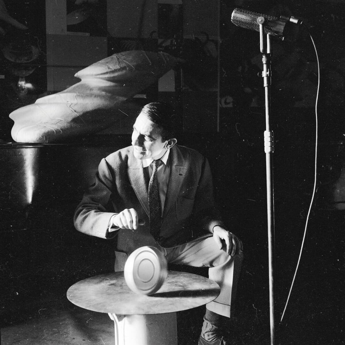 Une photo en noir et blanc montre un homme assis à une table, à côté d'un microphone.