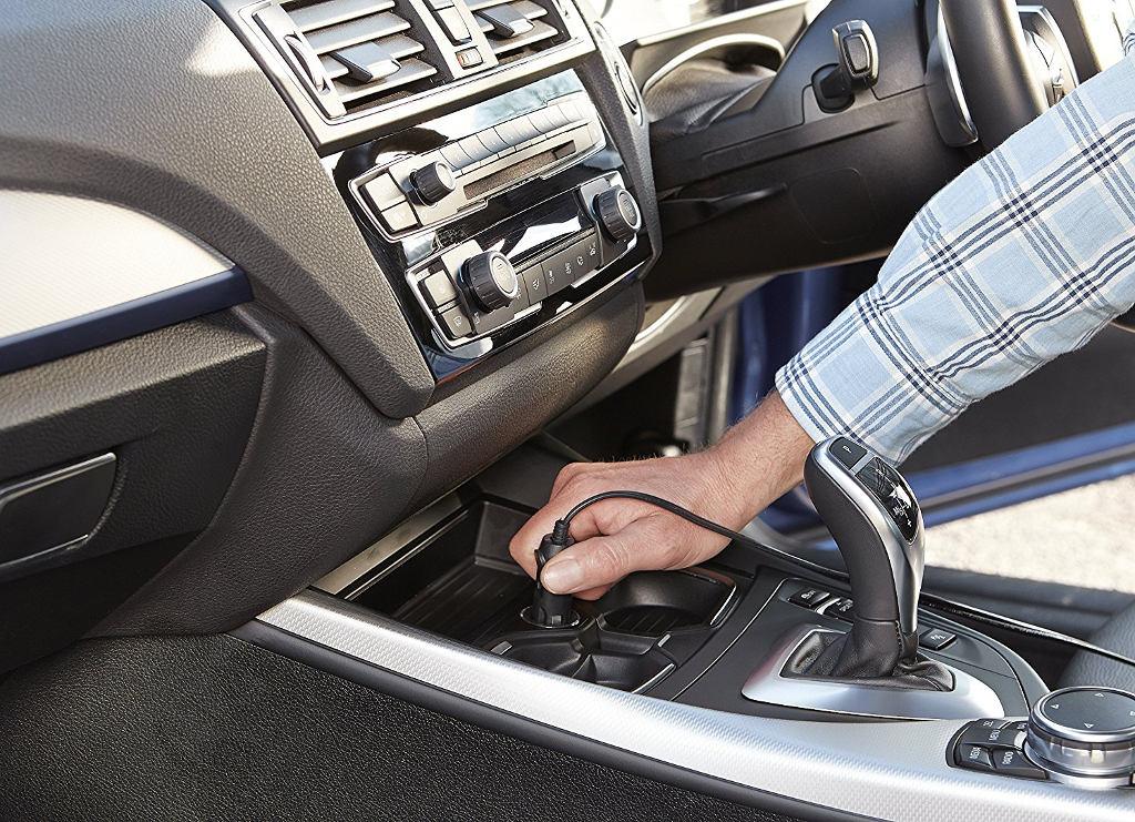 Egy kéz bedug egy autós töltőt az autó konzoljába.