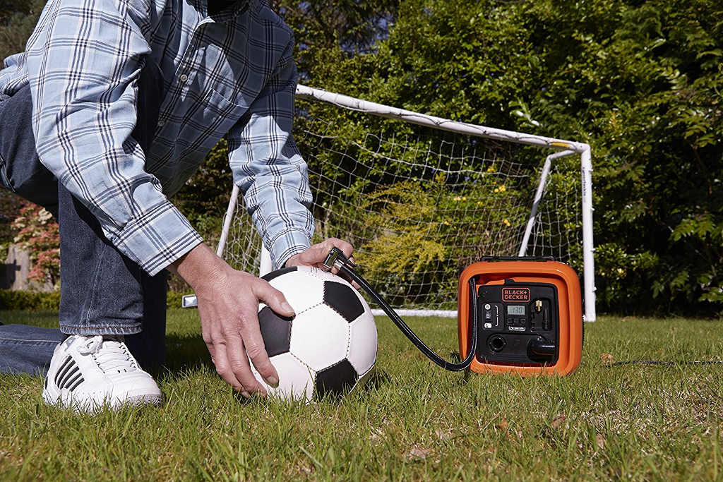 Egy személy focilabdát pumpál fekete-narancs színű pumpával.