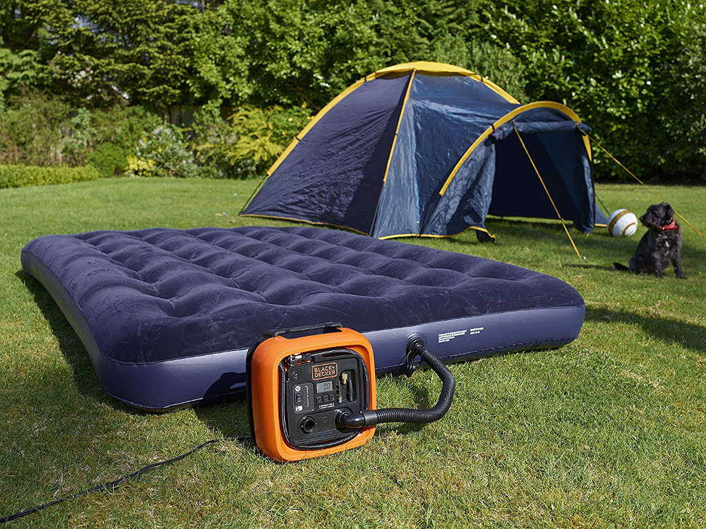 Egy felfújható matrac, egy sátor és egy áramforrás egy zöld gyepen kutyával.