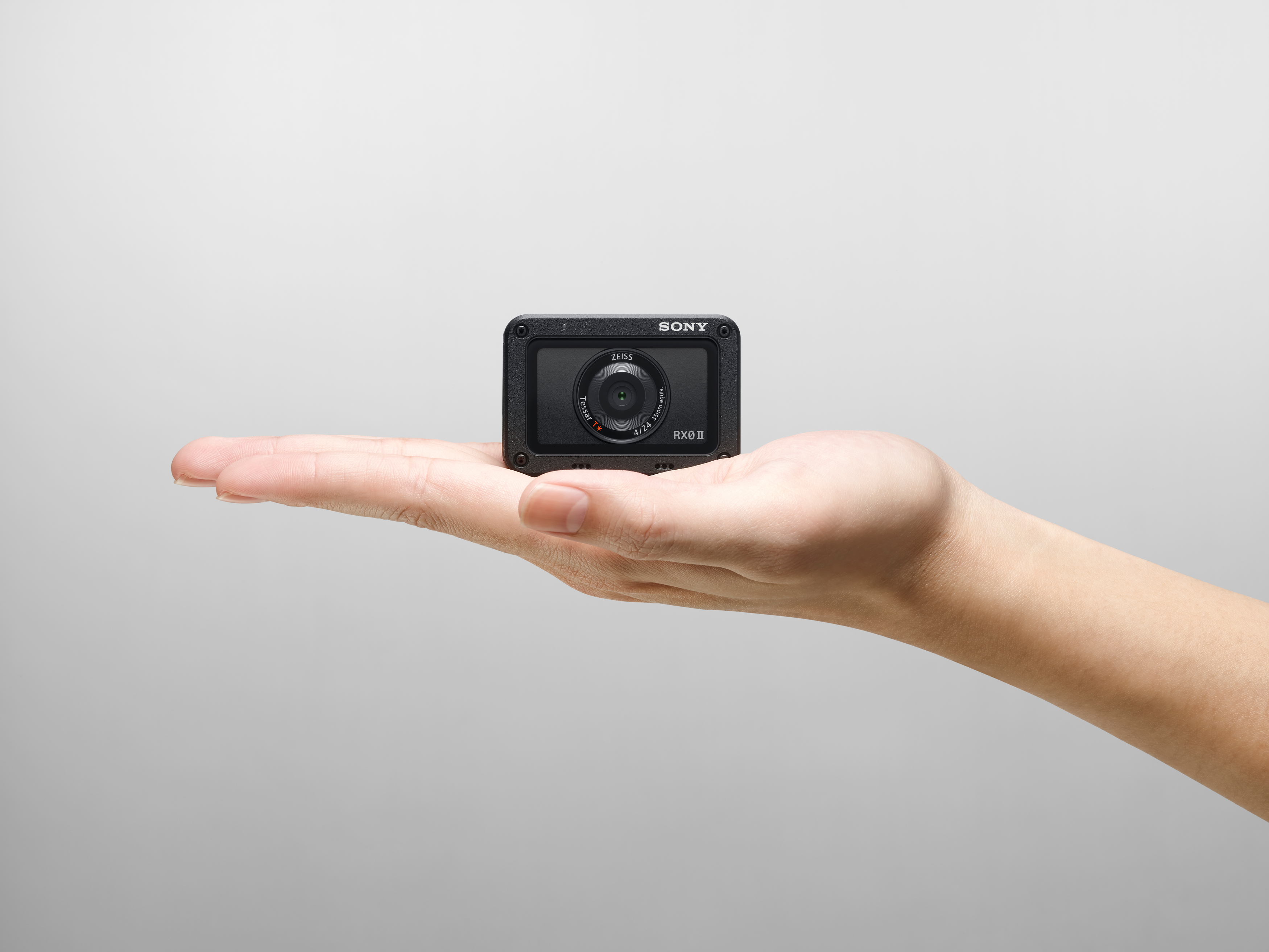 Eine kleine schwarze Kamera in der Hand. Die Kamera hat ein Zeiss-Objektiv und das Sony-Logo.