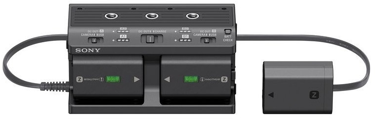 Chargeur de batterie Sony avec deux batteries insérées et une troisième batterie, le tout sur une surface grise.