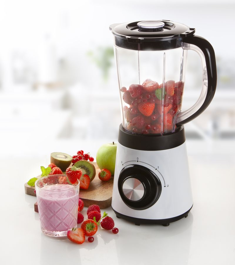 Mixeur rempli de fraises, de kiwi et un verre de smoothie rose.