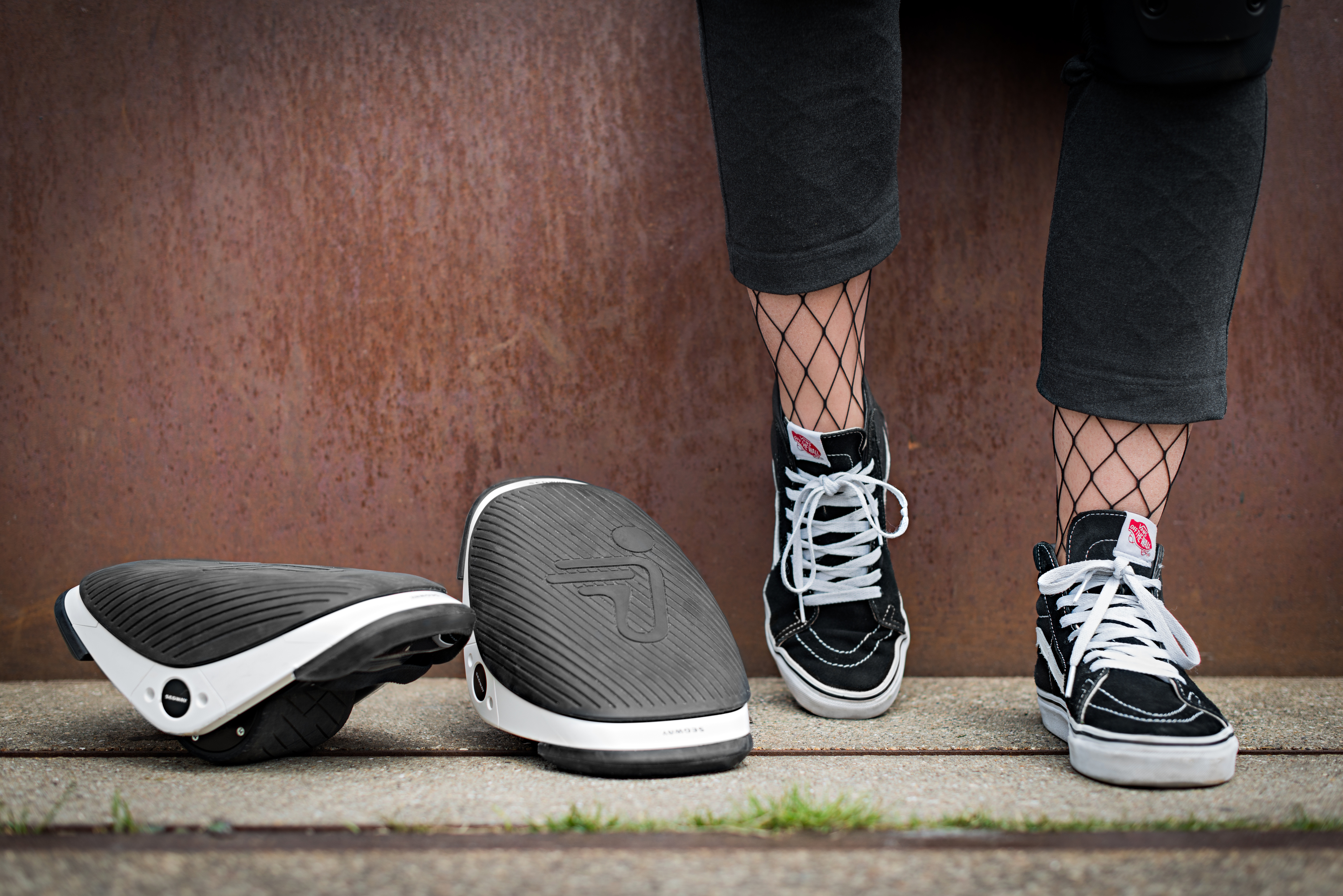 Beine einer Person mit Netzstrümpfen und Turnschuhen, in der Nähe von zwei Elektro-Rollschuhen.