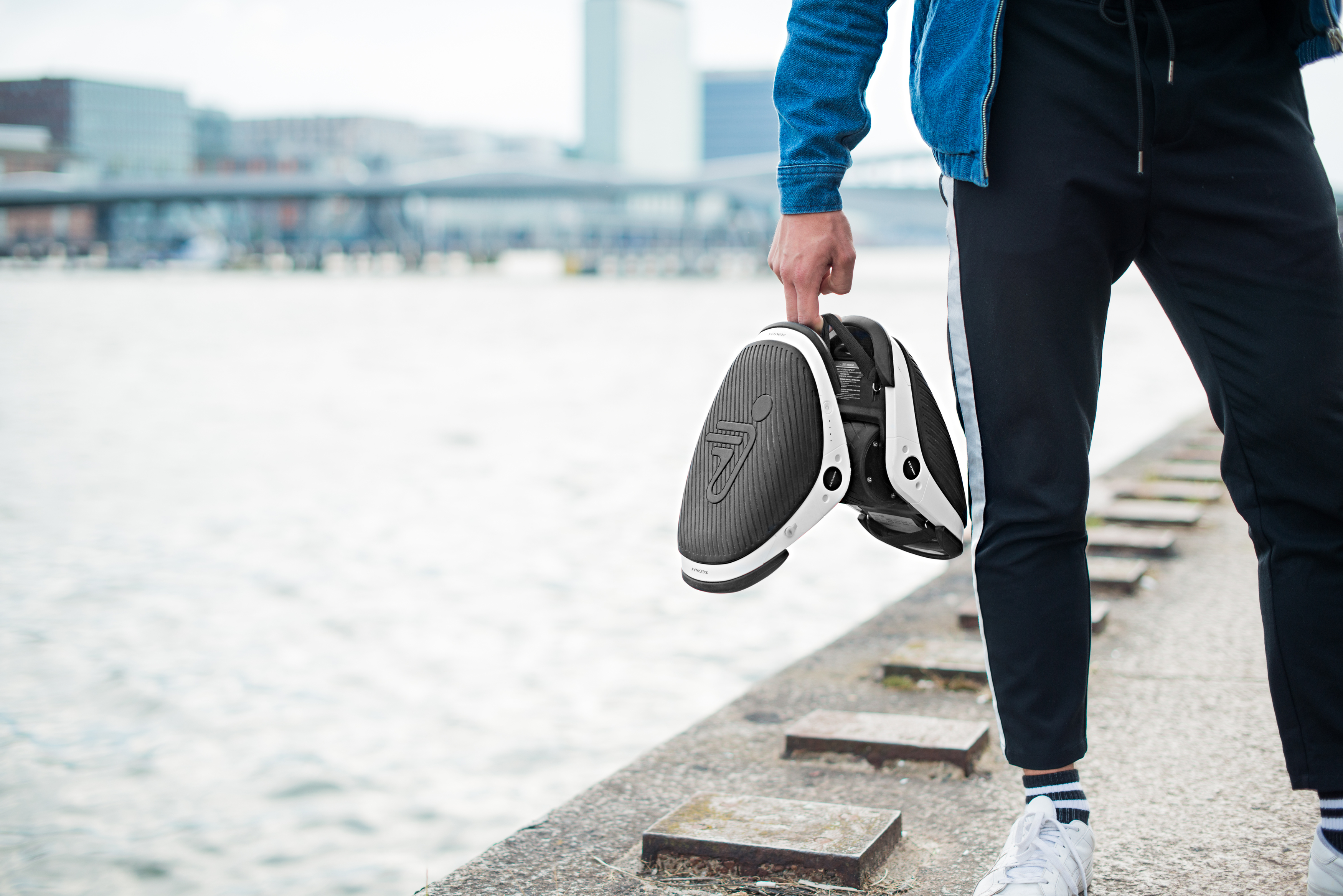 Person hält Segway-Schuhe. Sie sind schwarz und weiß. Stadt im Hintergrund.