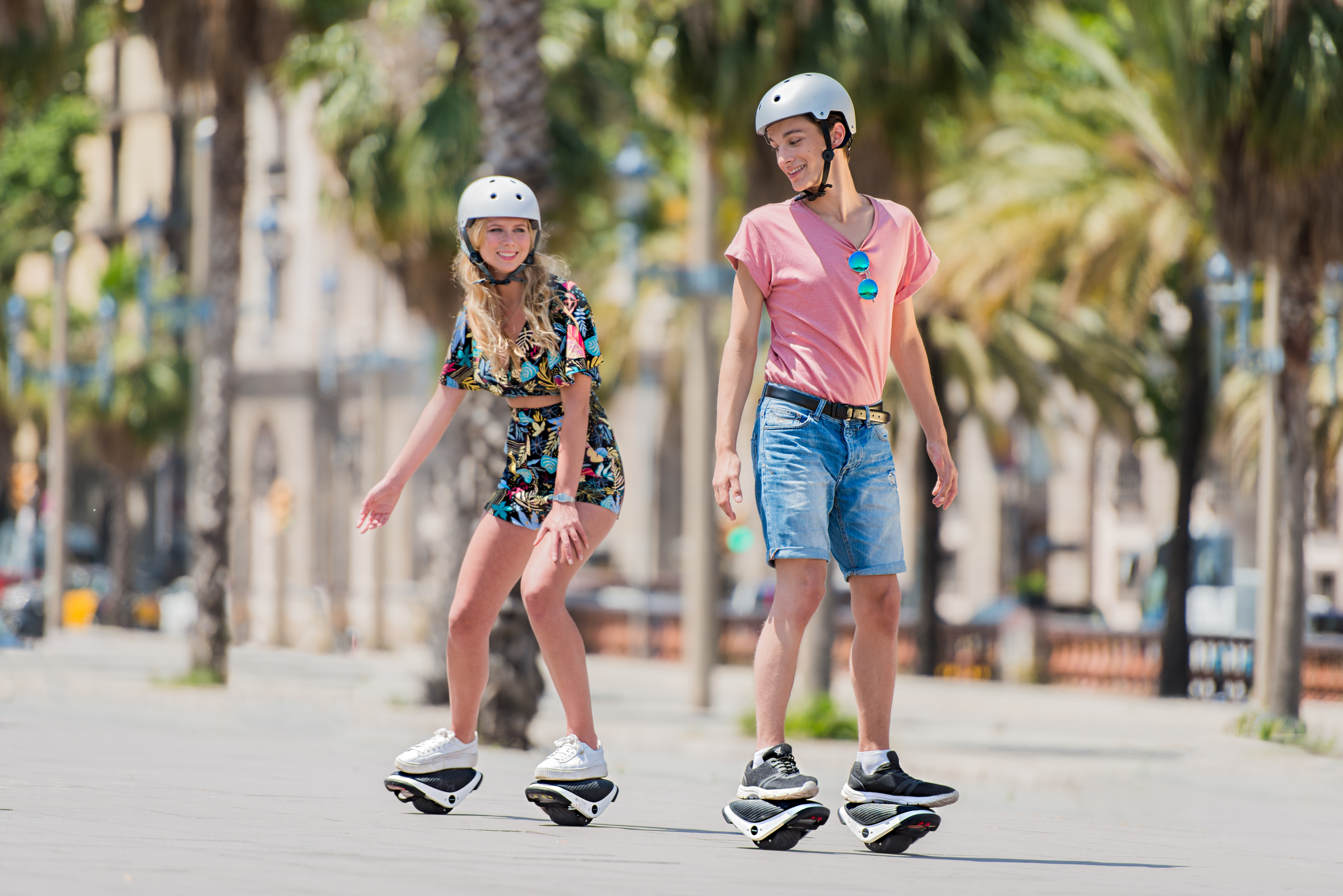 Zwei Personen auf Hoverboards fahren auf einem Bürgersteig in der Stadt.