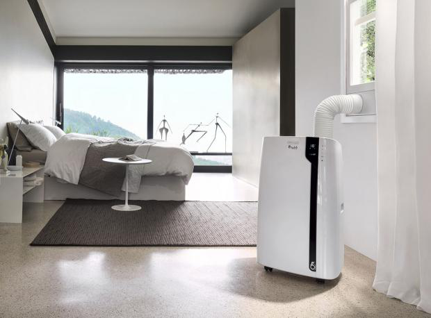 Condizionatore portatile bianco in una camera da letto vicino a una finestra con vista.