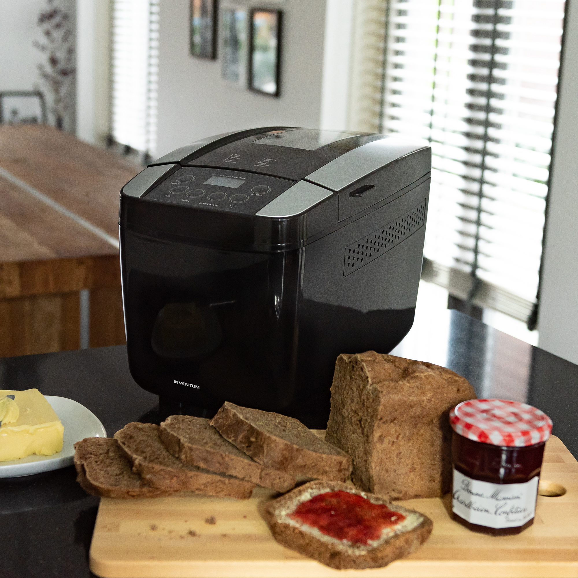 Zwarte broodbakmachine met gesneden brood, jam en boter op een houten plank.