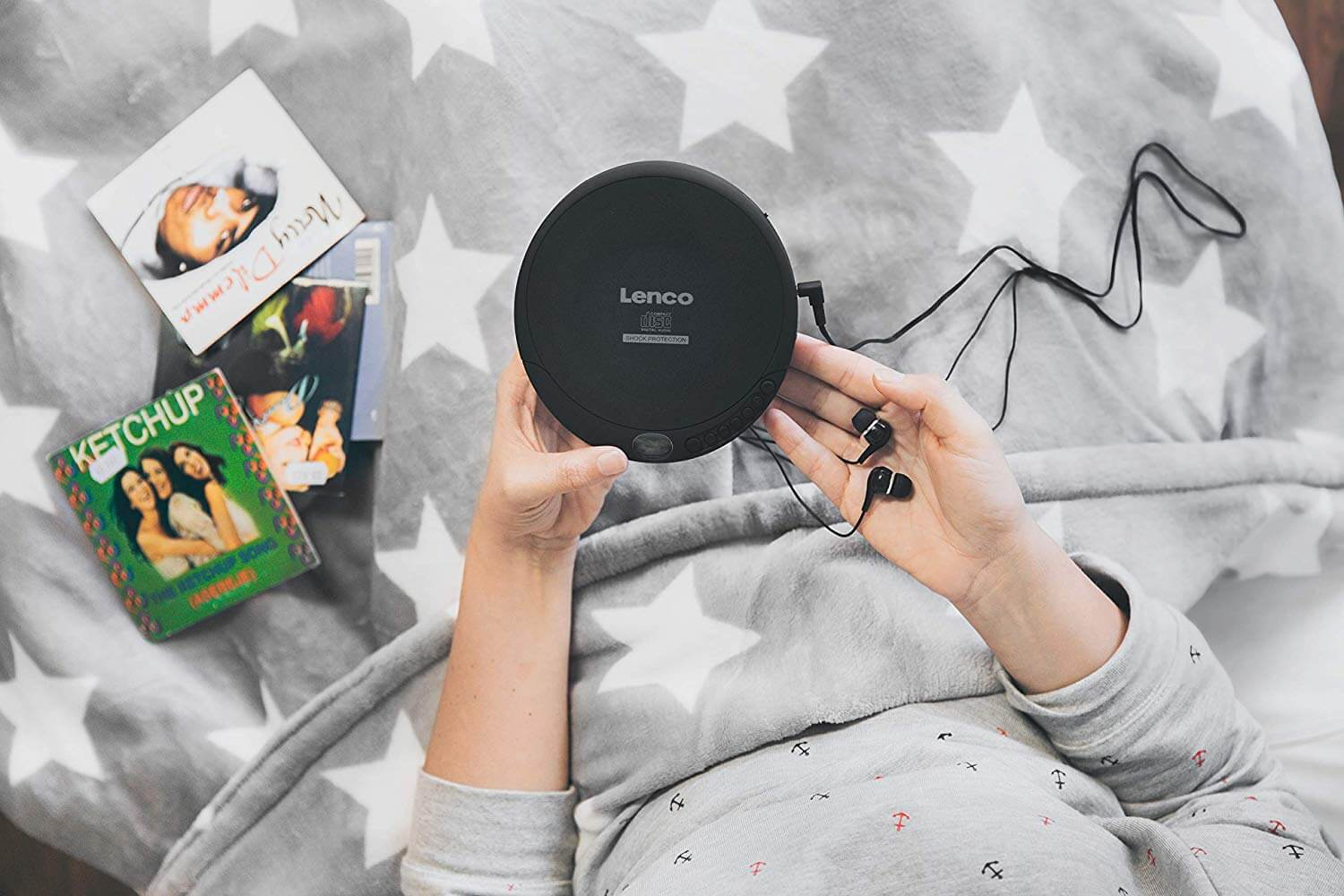 A person holding a black Lenco CD player with headphones, CDs are in the background, top view.