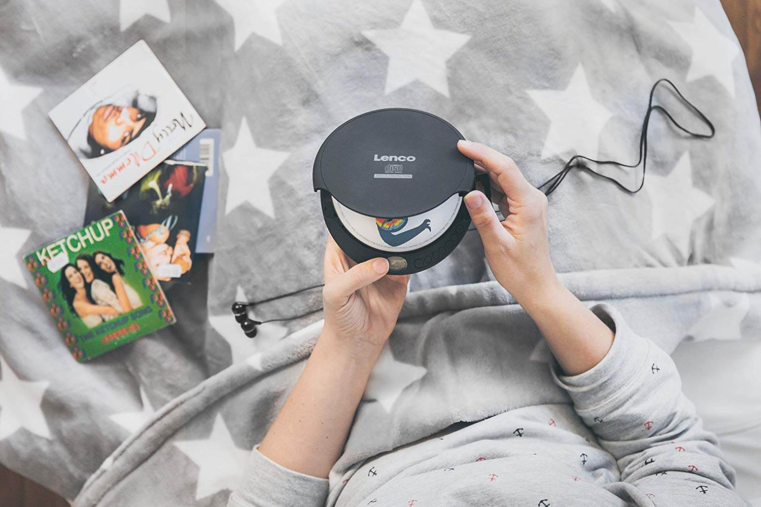 A person holding a black Lenco CD player and several CD album covers on a bed.