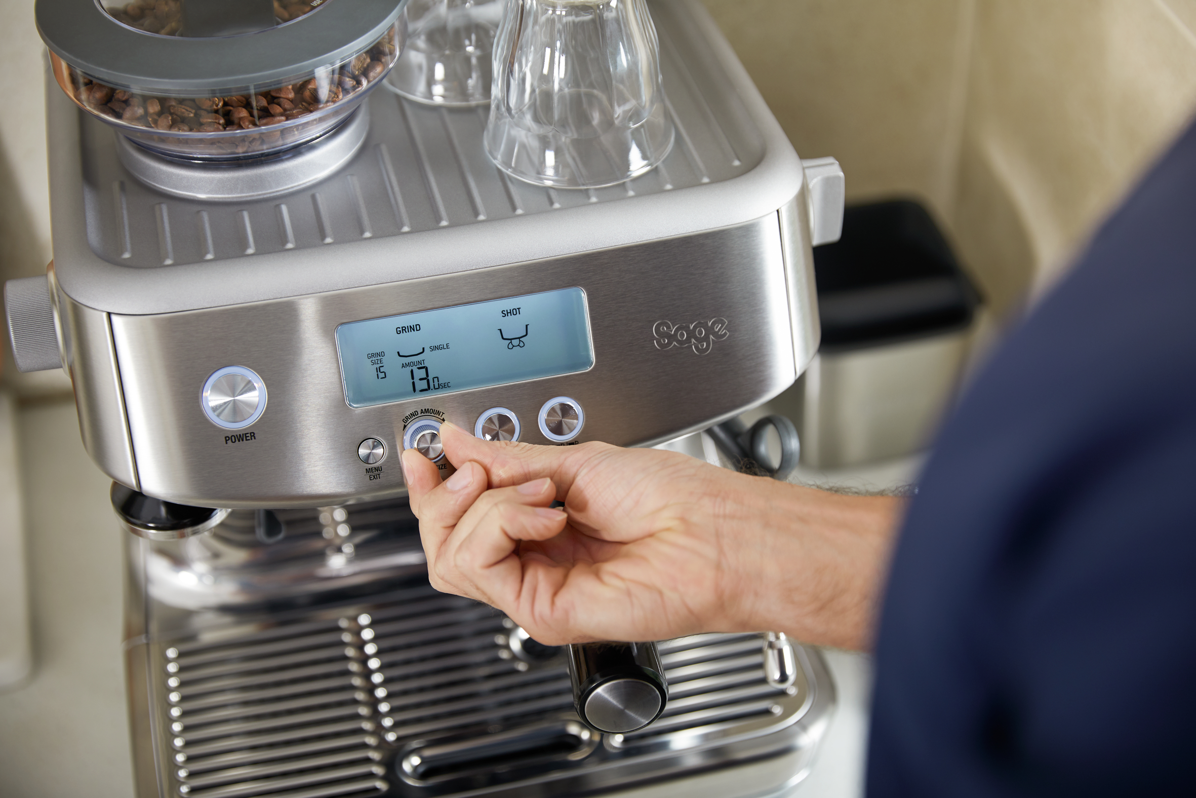 Hand einer Person, die die Einstellungen an einer silbernen Kaffeemaschine mit digitaler Anzeige anpasst.