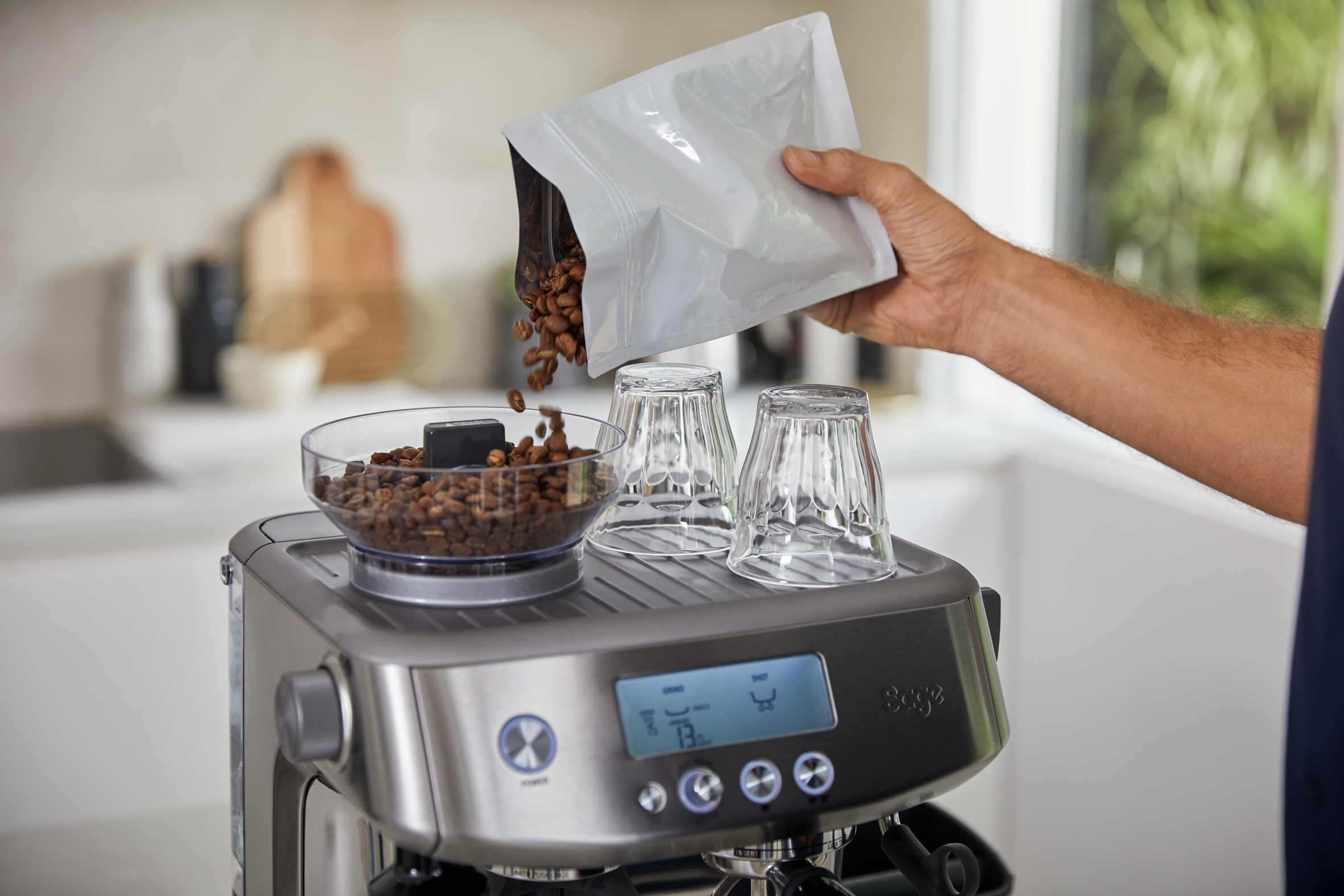 Kaffeebohnen werden aus einem Beutel in eine Schüssel auf einer silbernen Espressomaschine gegossen.
