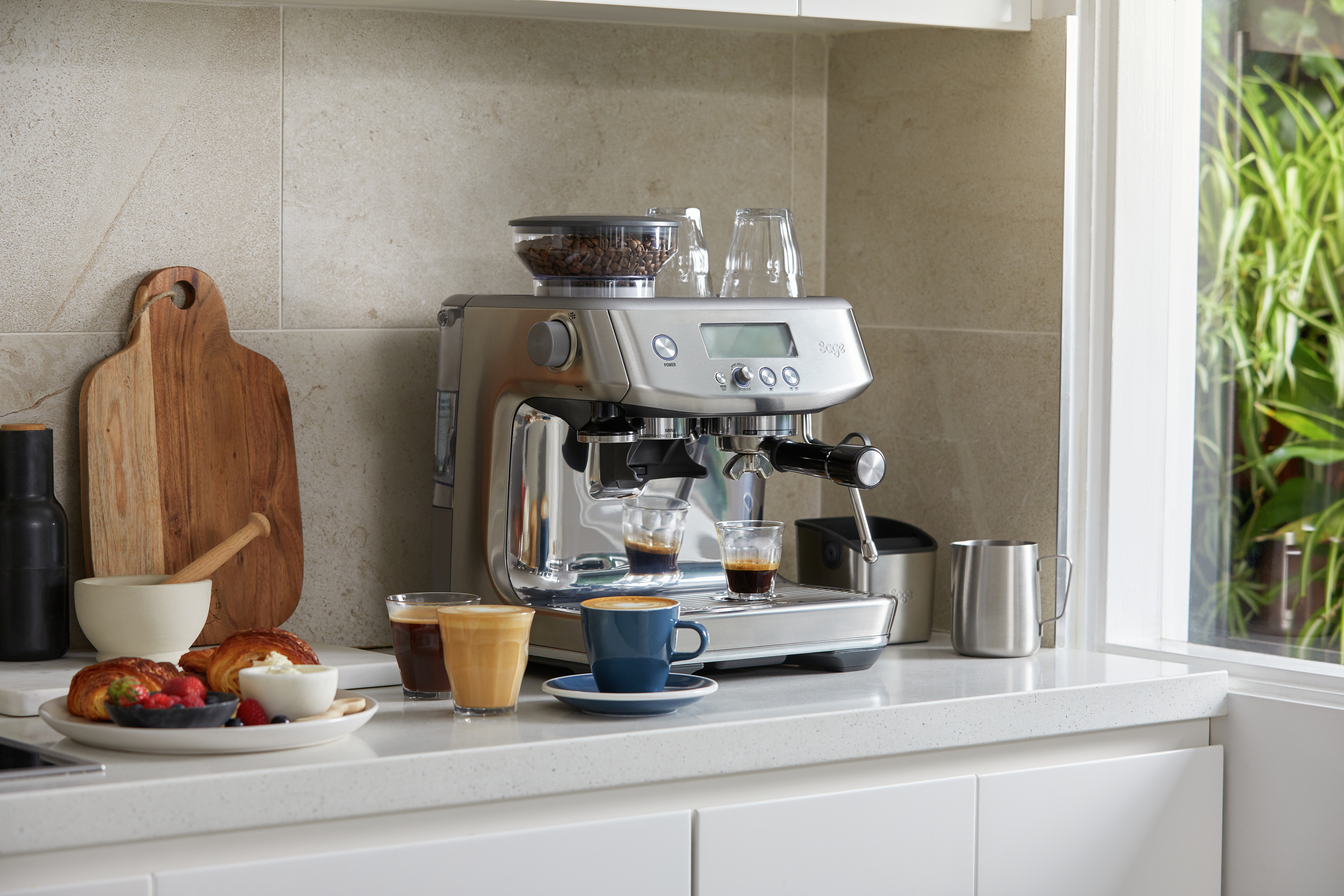 Eine Espressomaschine aus Edelstahl auf einer weißen Arbeitsplatte mit Kaffee und Gebäck.