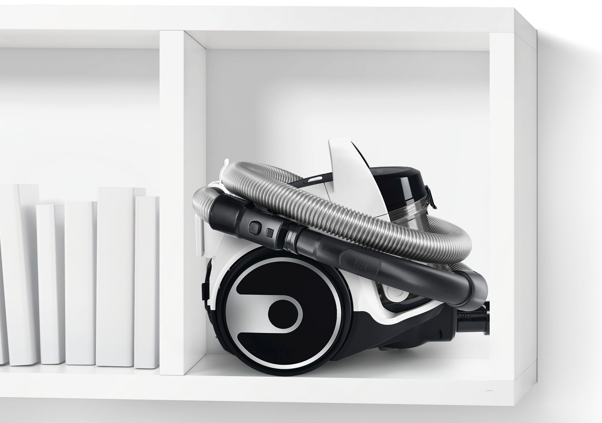 White vacuum cleaner is stored on a white shelf. A few white books are on the left.