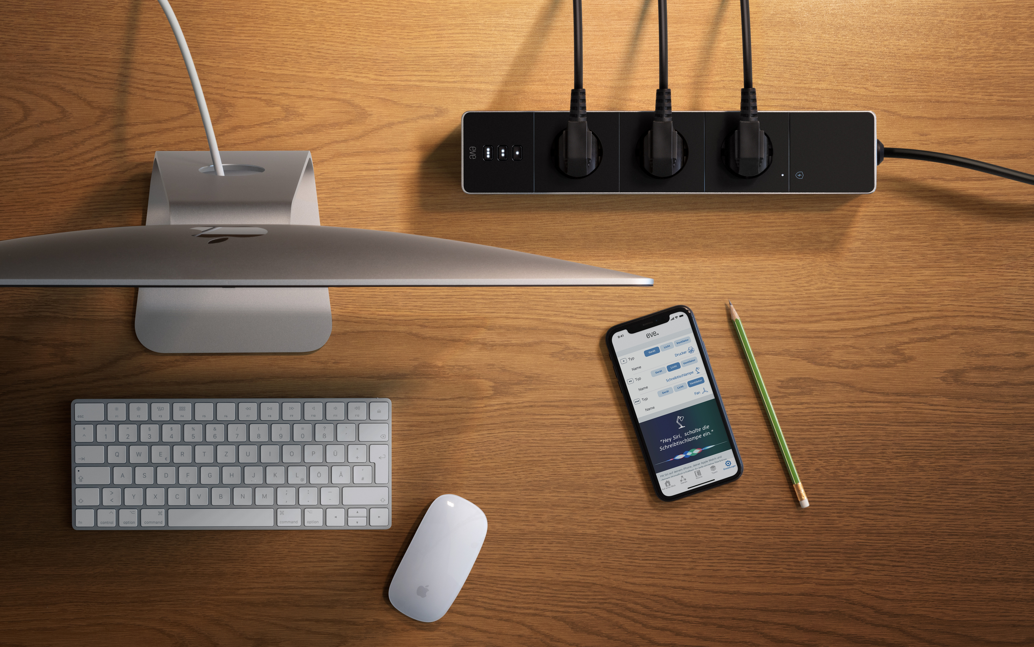 Ein Holzschreibtisch mit Computerzubehör: Monitor, Tastatur, Maus, Steckdosenleiste und Telefon.