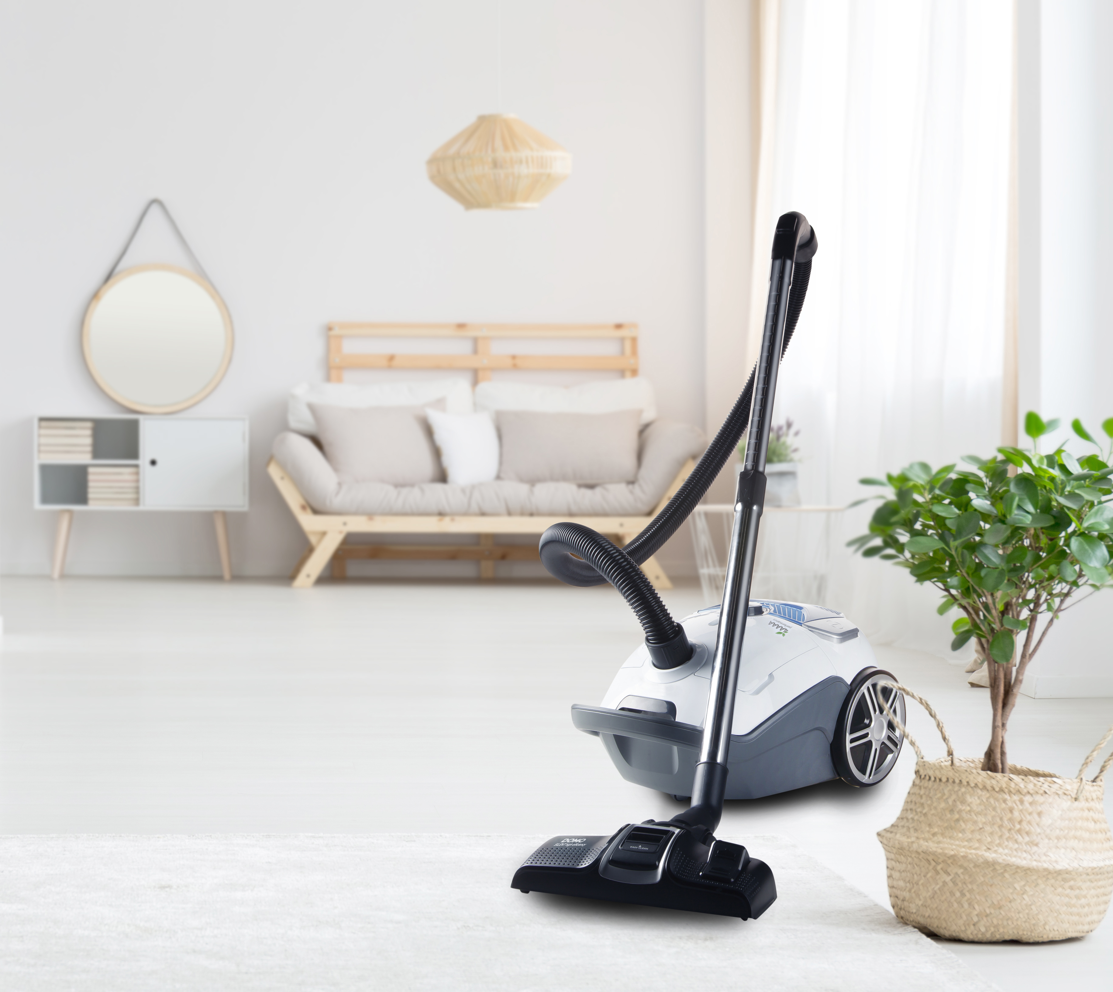 Een witte en grijze stofzuiger staat op een wit tapijt, in een woonkamer met neutrale inrichting.