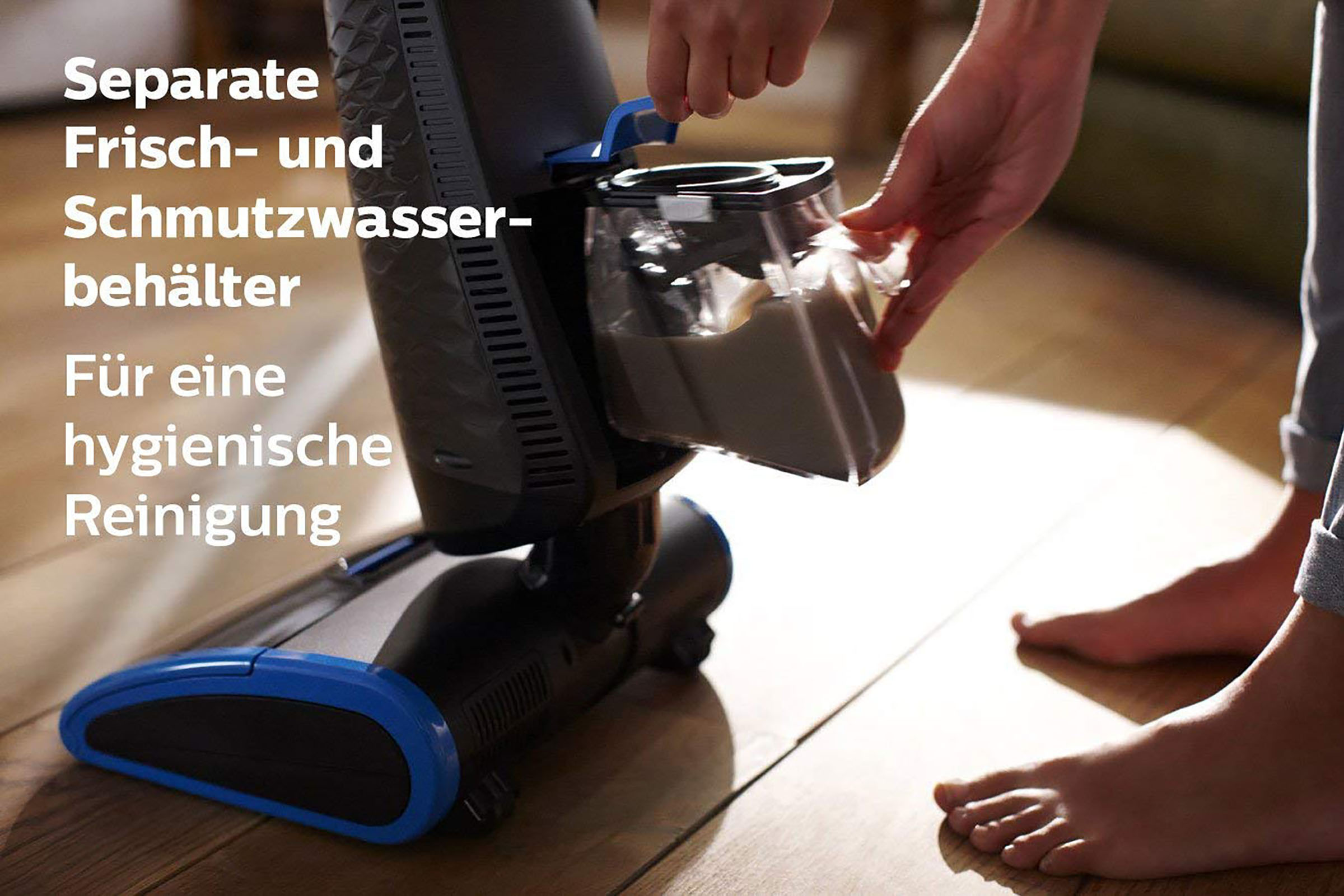 Eine Person entfernt einen Schmutzwasserbehälter von einem Staubsauger. Barfuß im Vordergrund, Parkettboden im Hintergrund.