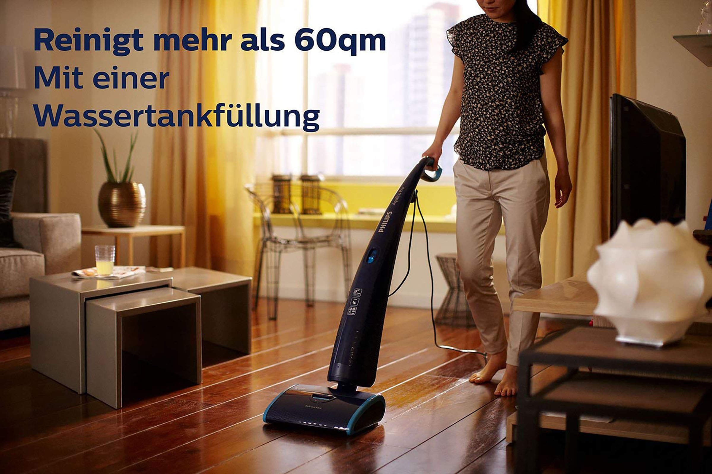 Eine Frau benutzt einen Philips AquaTrio Pro Staubsauger auf einem Hartholzboden. Der Raum hat ein Sofa und Tische.