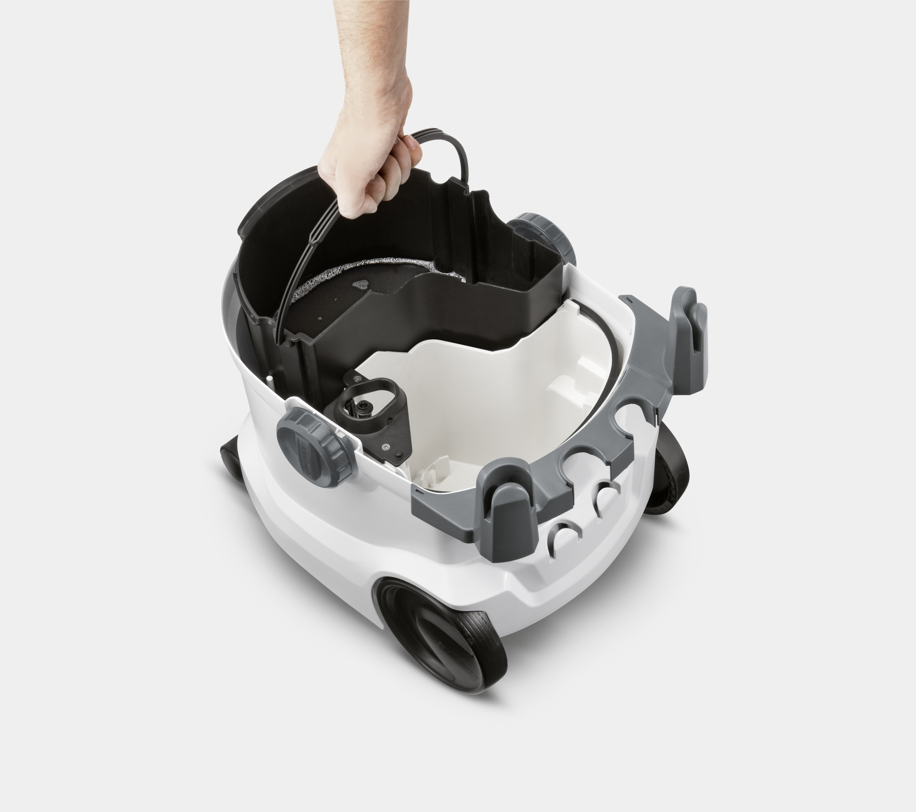 Eine Hand, die den herausnehmbaren Behälter eines Staubsaugers hält, die Maschine ist geöffnet.