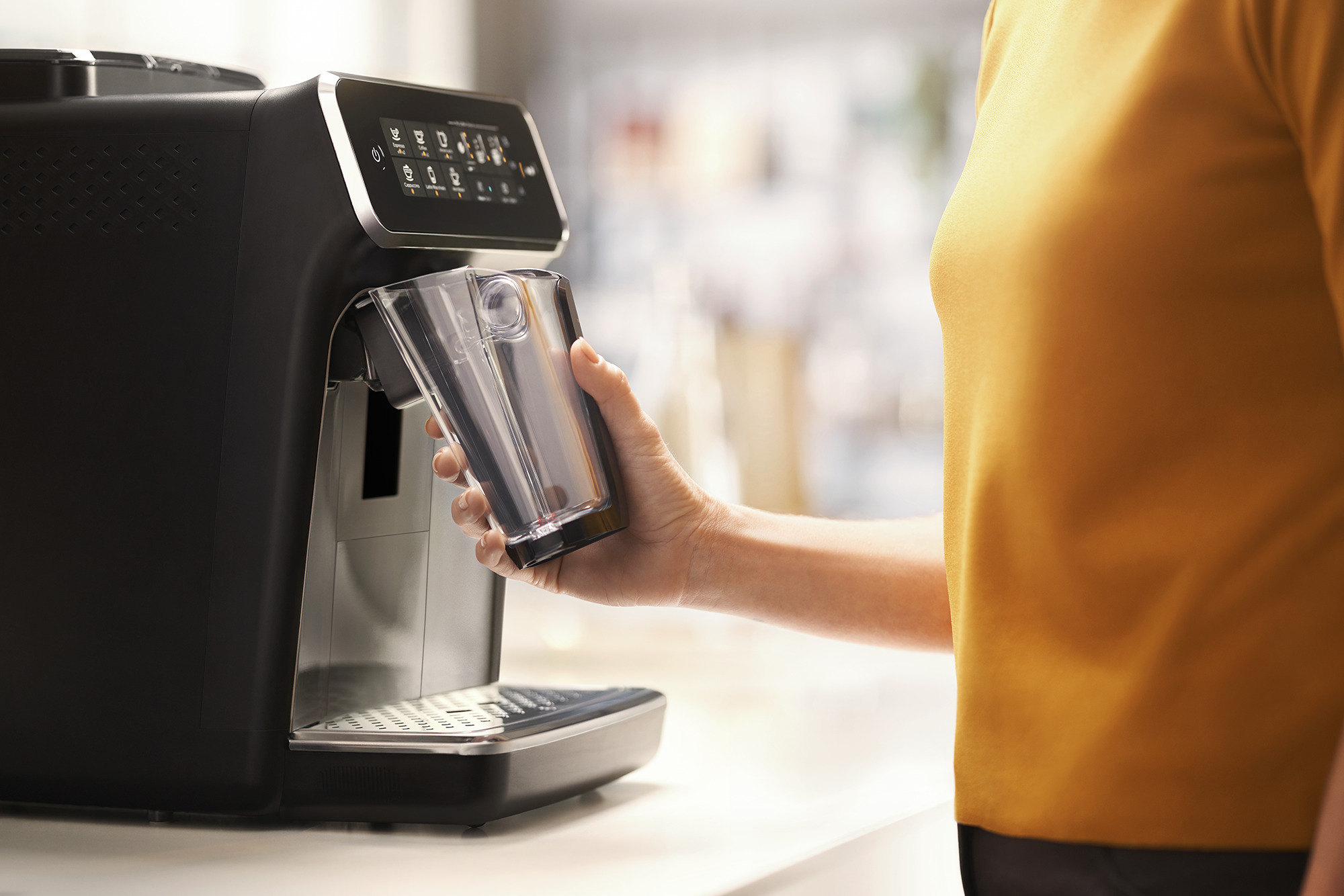 A woman is using an espresso machine. She is holding a glass with a black base.