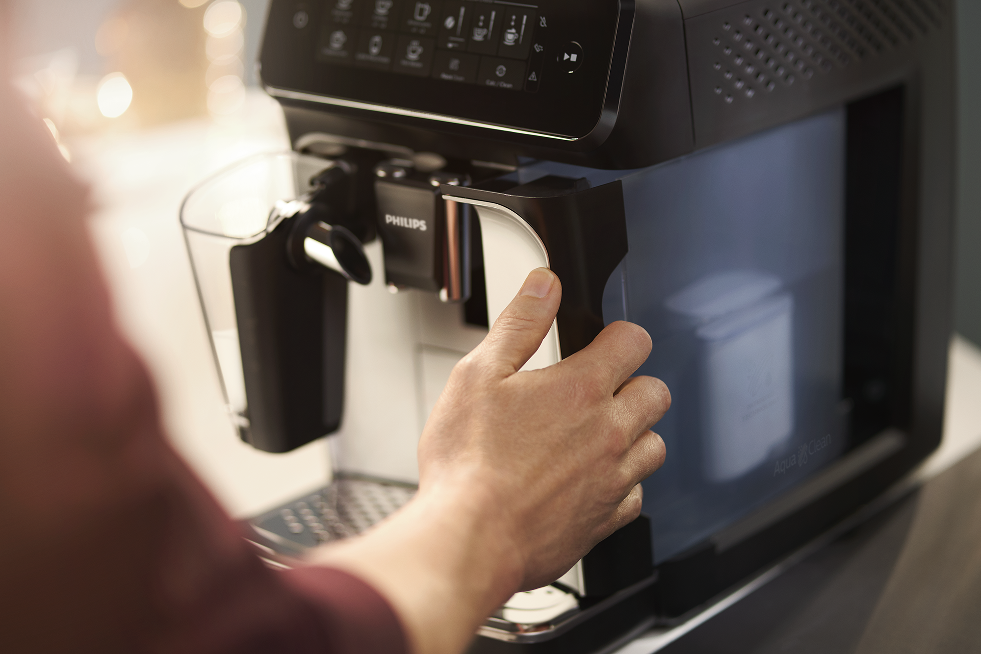 Person adding water to a black and silver Philips coffee machine. The background is blurry.