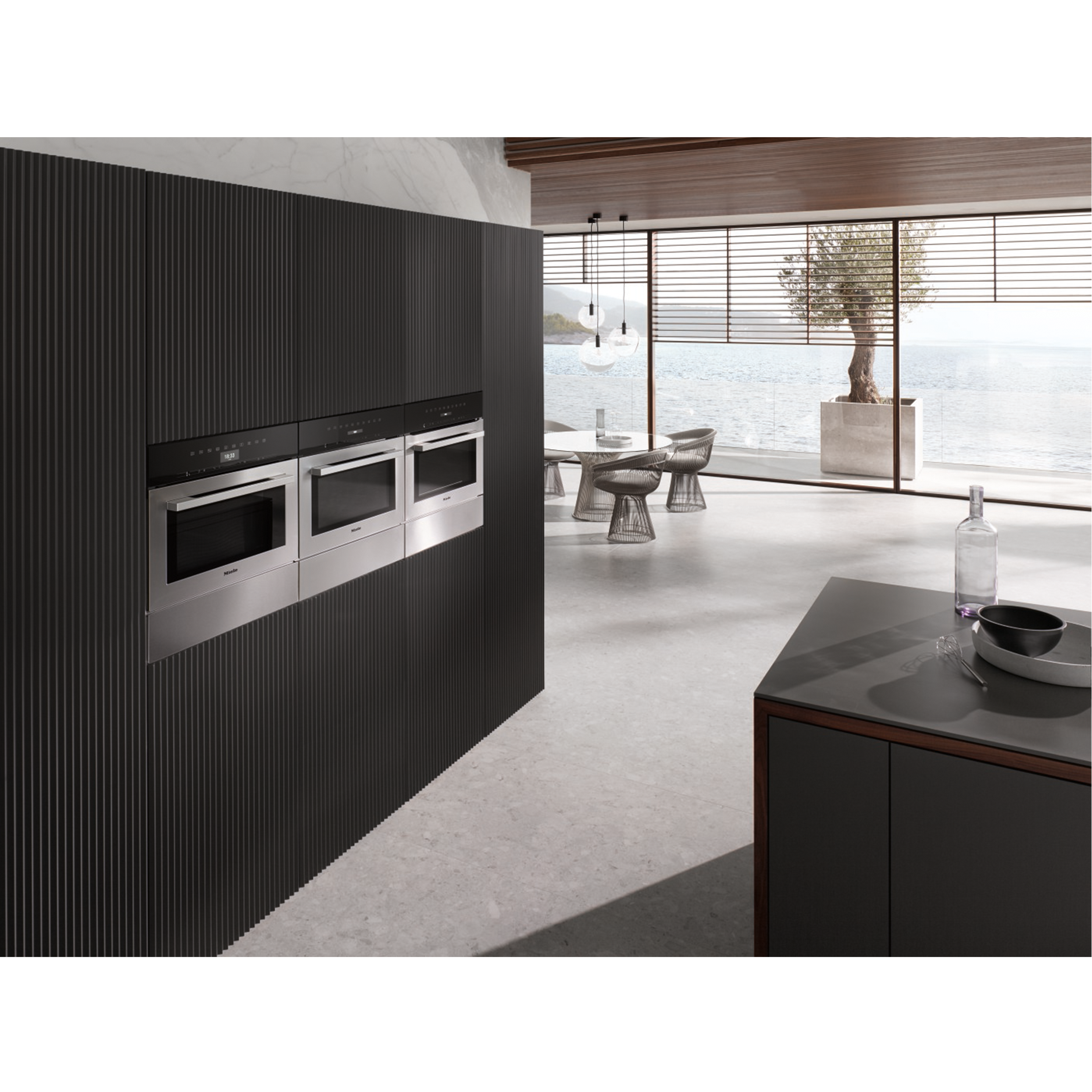 Modern kitchen with black cabinets and three ovens. Dining area overlooking the sea.