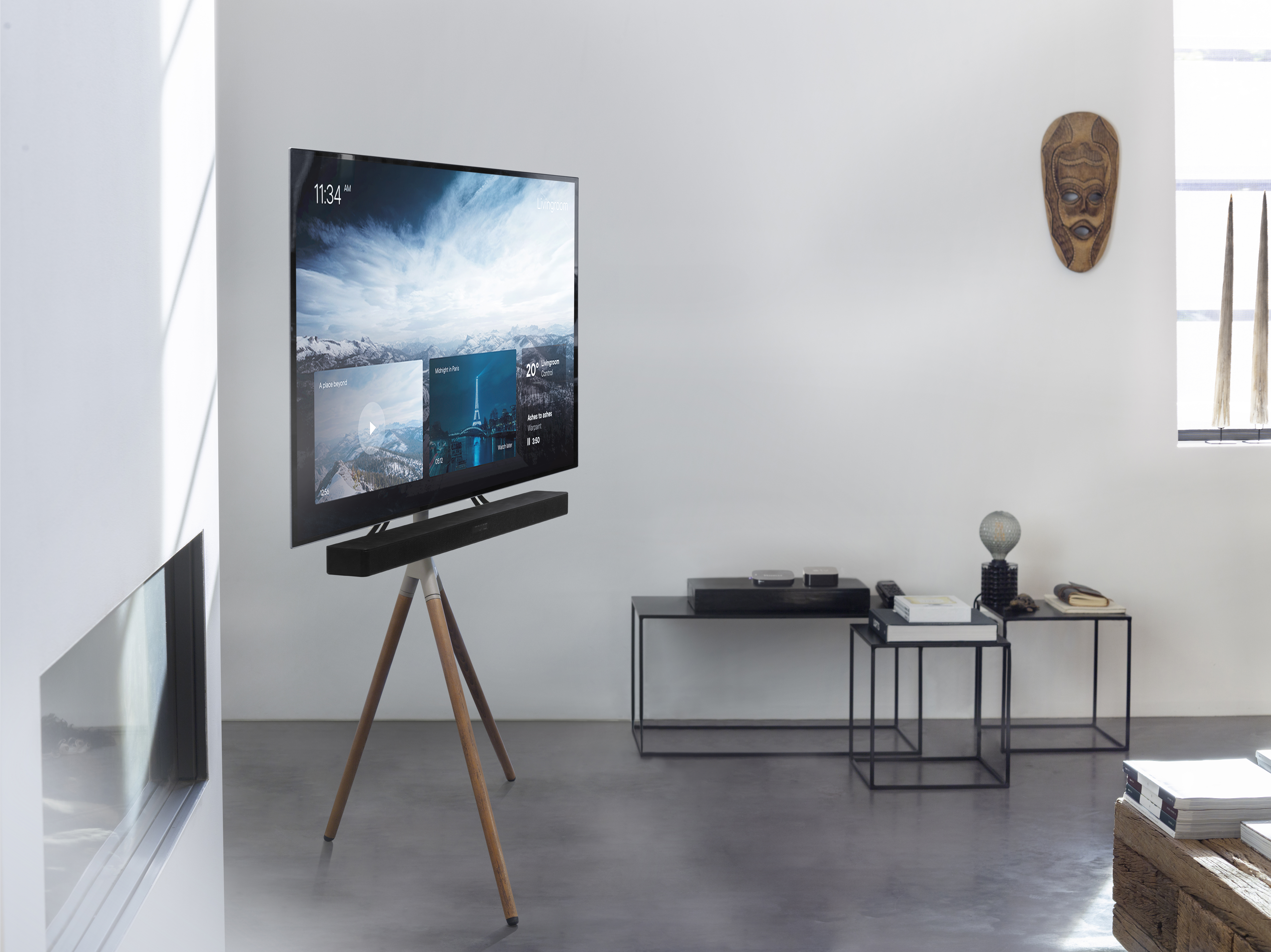 Ein Fernseher auf einem Ständer mit Holzbeinen in einem weißen Raum. Ein Kamin ist sichtbar.