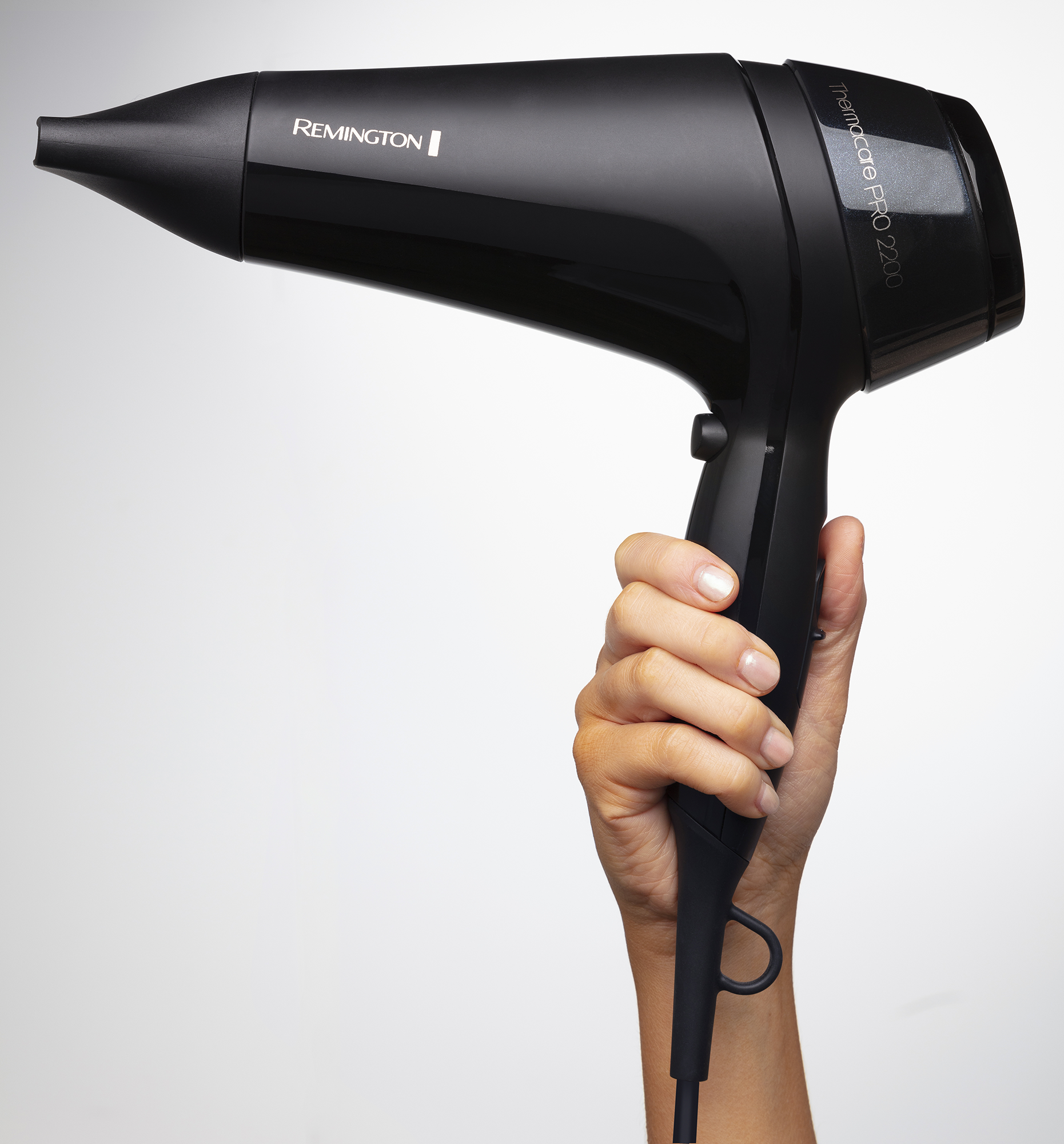A hand holding a black Remington hair dryer against a white backdrop. The dryer is on.