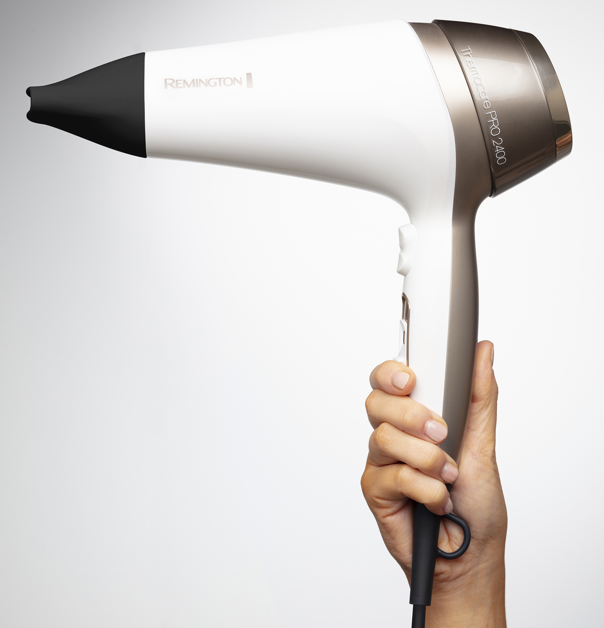 A hand holds a white and gold hair dryer. It has the Remington and Trimmer Pro logos.
