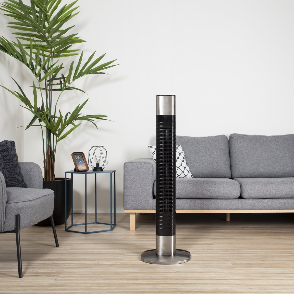 Vloerventilator in moderne stijl in een woonkamer. Grijze bank, planten en een bijzettafel.