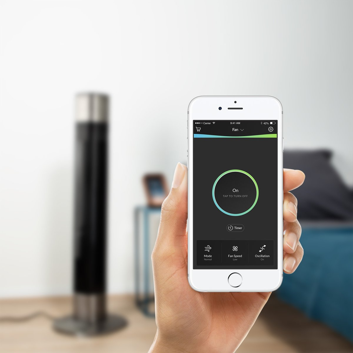 Een hand die een telefoon vasthoudt met een app om een zwarte en zilveren ventilator te bedienen.