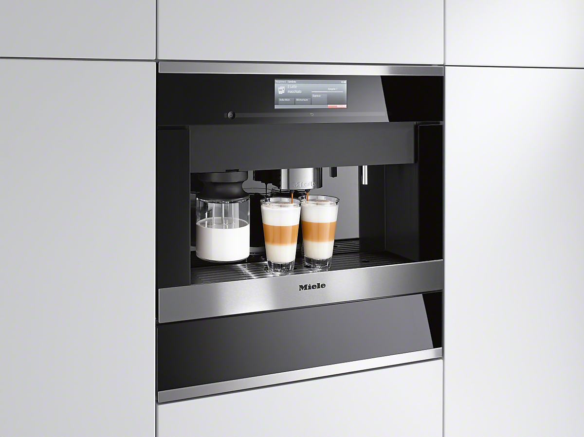 Eingebaute Miele Kaffeemaschine mit Latte-Gläsern. Weiße Schränke im Hintergrund.