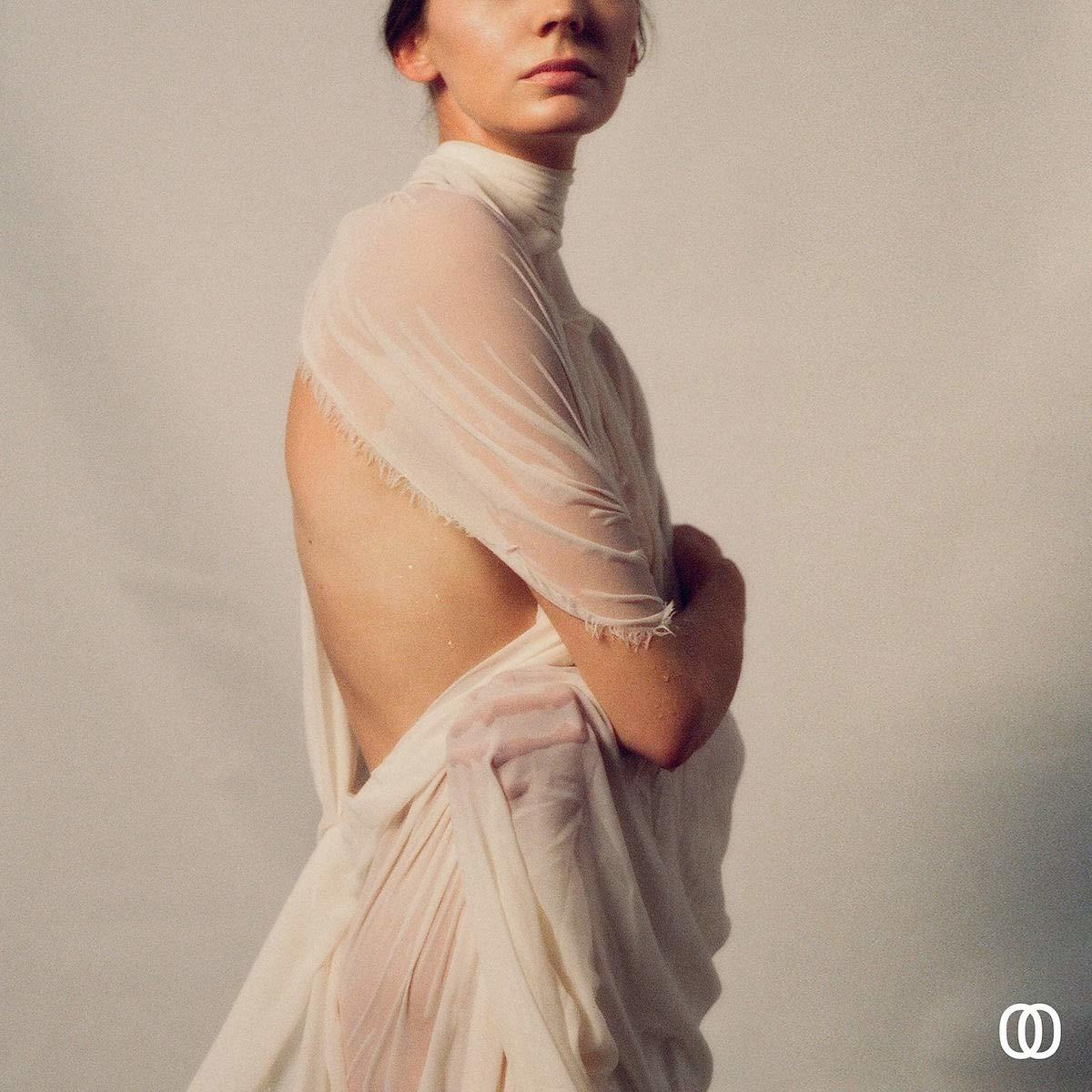 Femme en robe blanche dos nu, bras croisés.