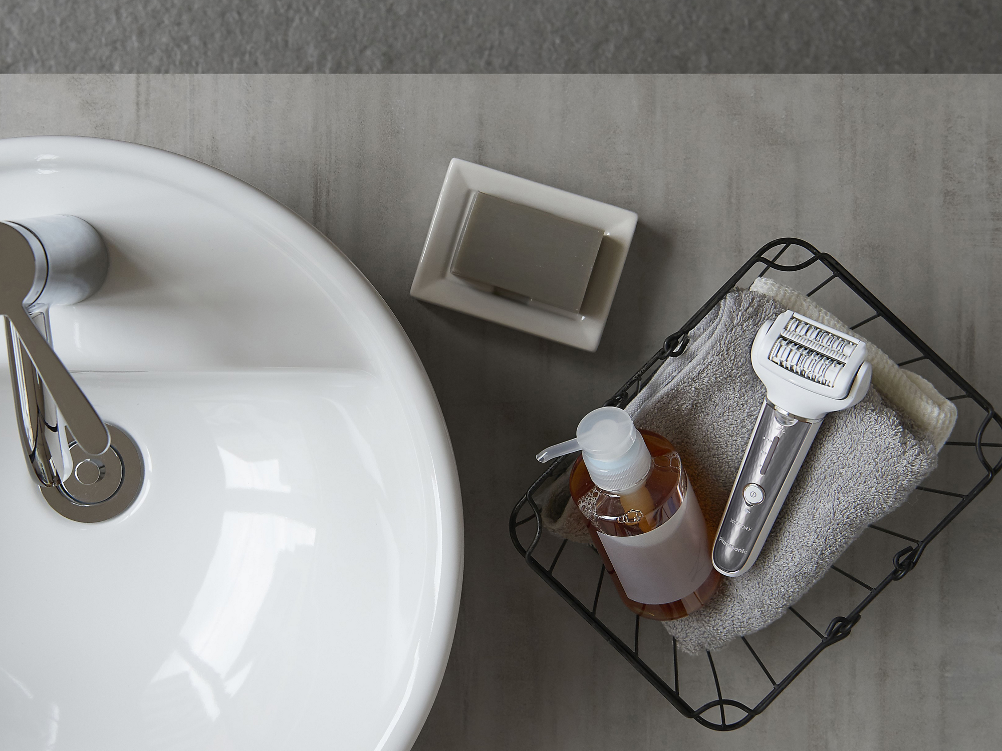 Espace lavabo avec savon, savon liquide et un épilateur dans un panier en fil de fer.