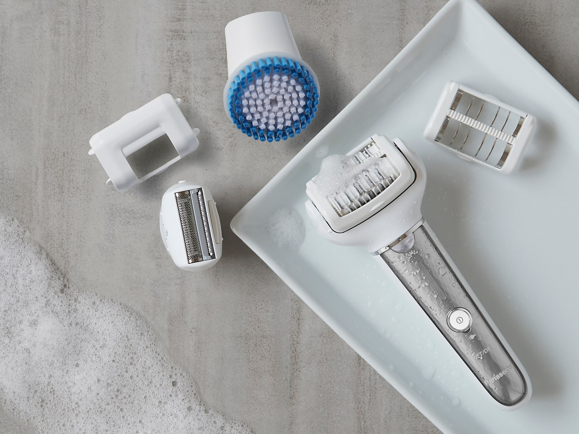 Un plateau blanc avec des composants de rasoir électrique démontés : tête, brosse et tête de coupe.
