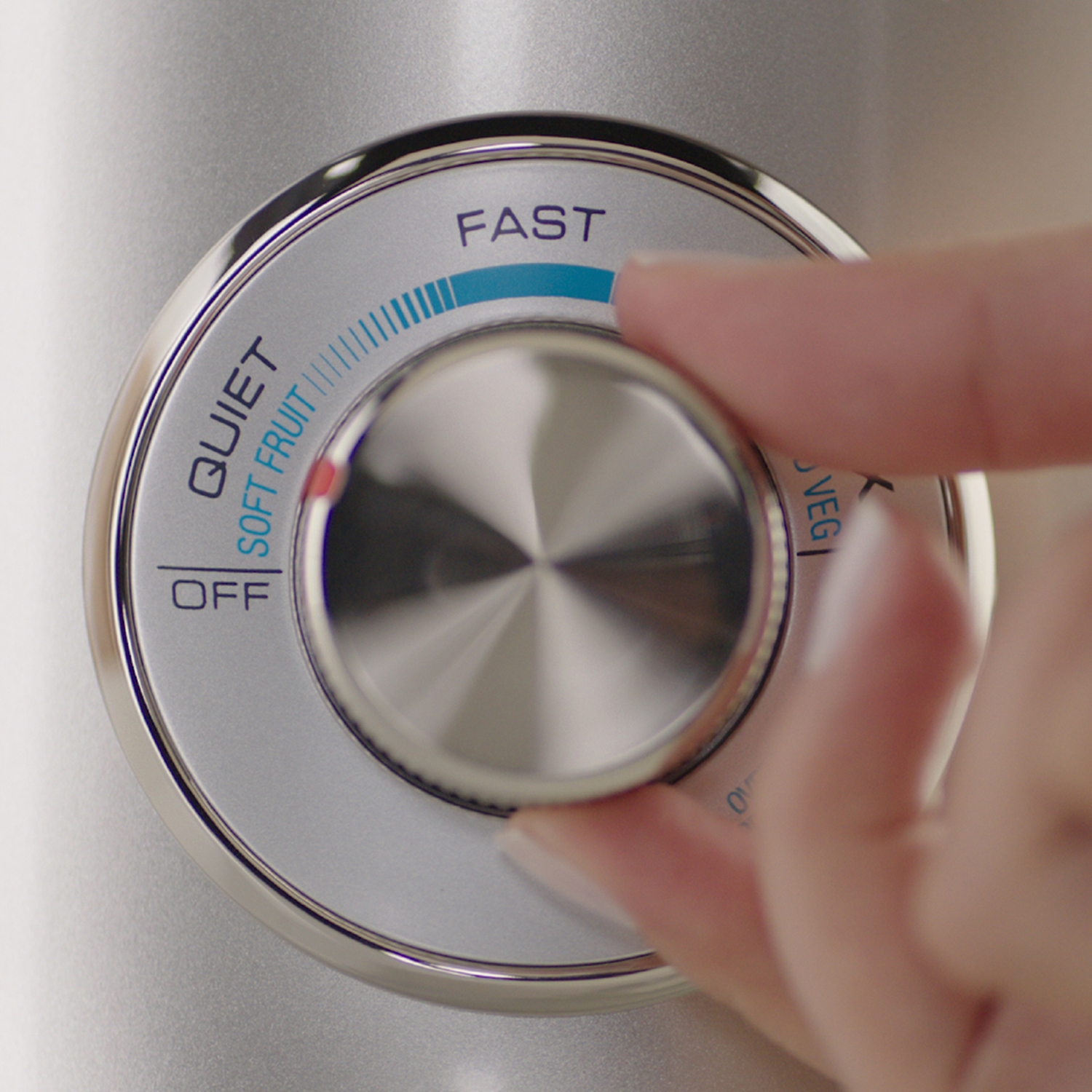 A silver blender control dial, hand adjusting to 'FAST'. The background is a silver surface.