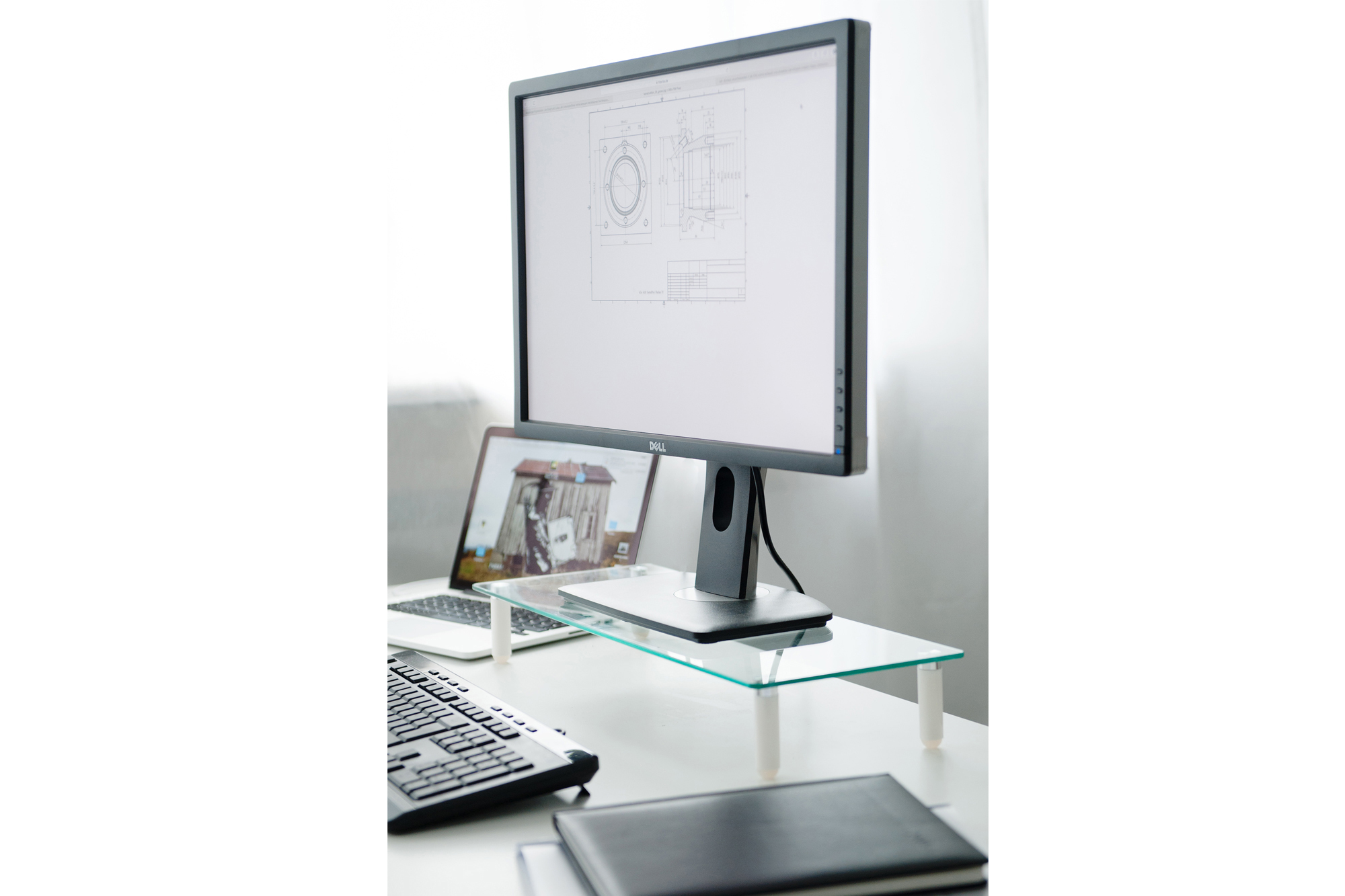 Ein Computer-Setup mit einem Monitor auf einem Glasständer, einem Laptop und einer Tastatur.