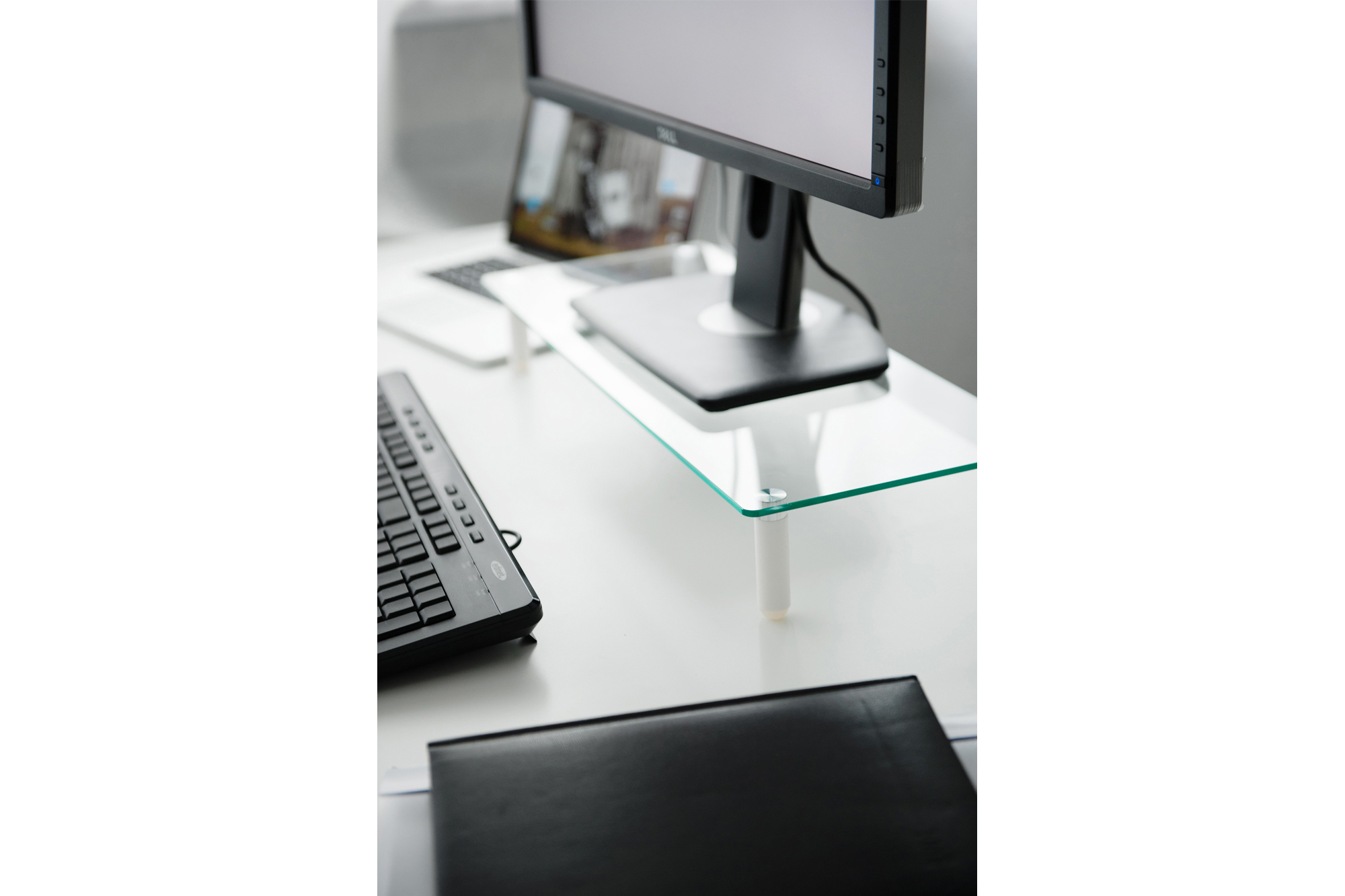 Ein Schreibtisch mit Monitor, Tastatur und Laptop. Ein Glasregal hält den Monitor.
