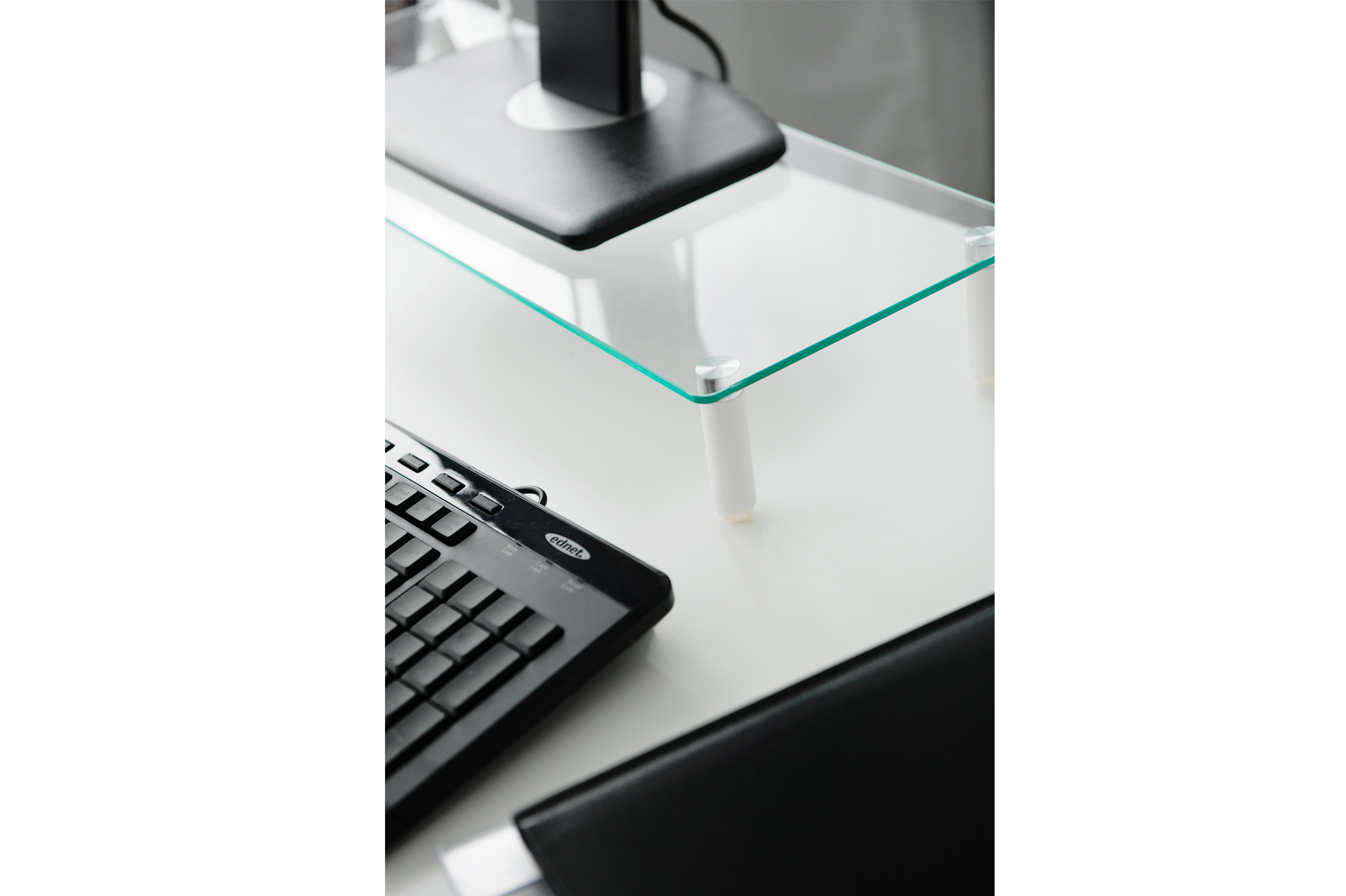 Glas-Monitorständer mit schwarzer Tastatur und Monitor. Der Schreibtisch ist weiß.