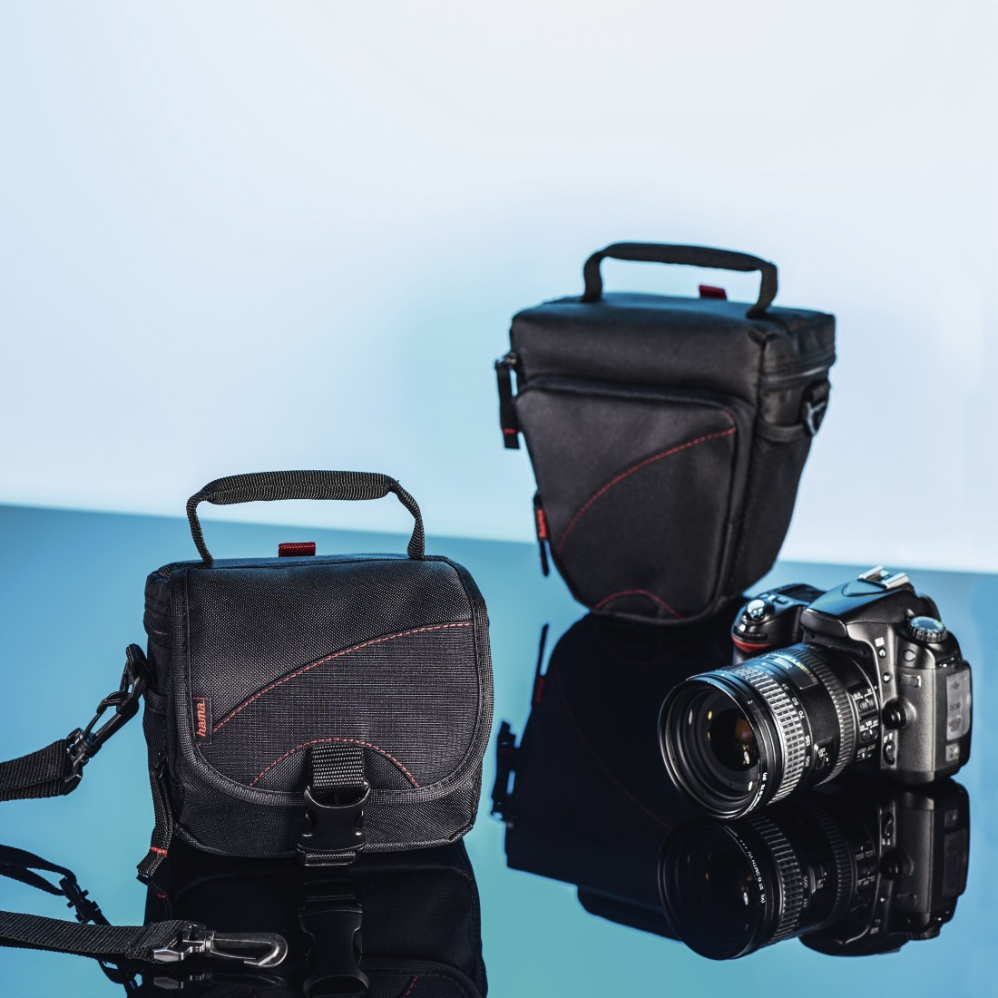 Borse nere per fotocamere e una fotocamera DSLR su una superficie riflettente contro uno sfondo blu sfumato.