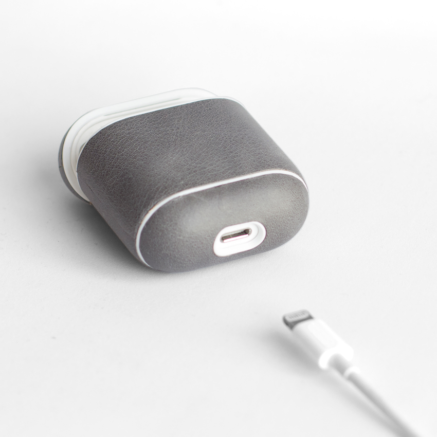 A gray case for AirPods with a white charging cable in front of it.
