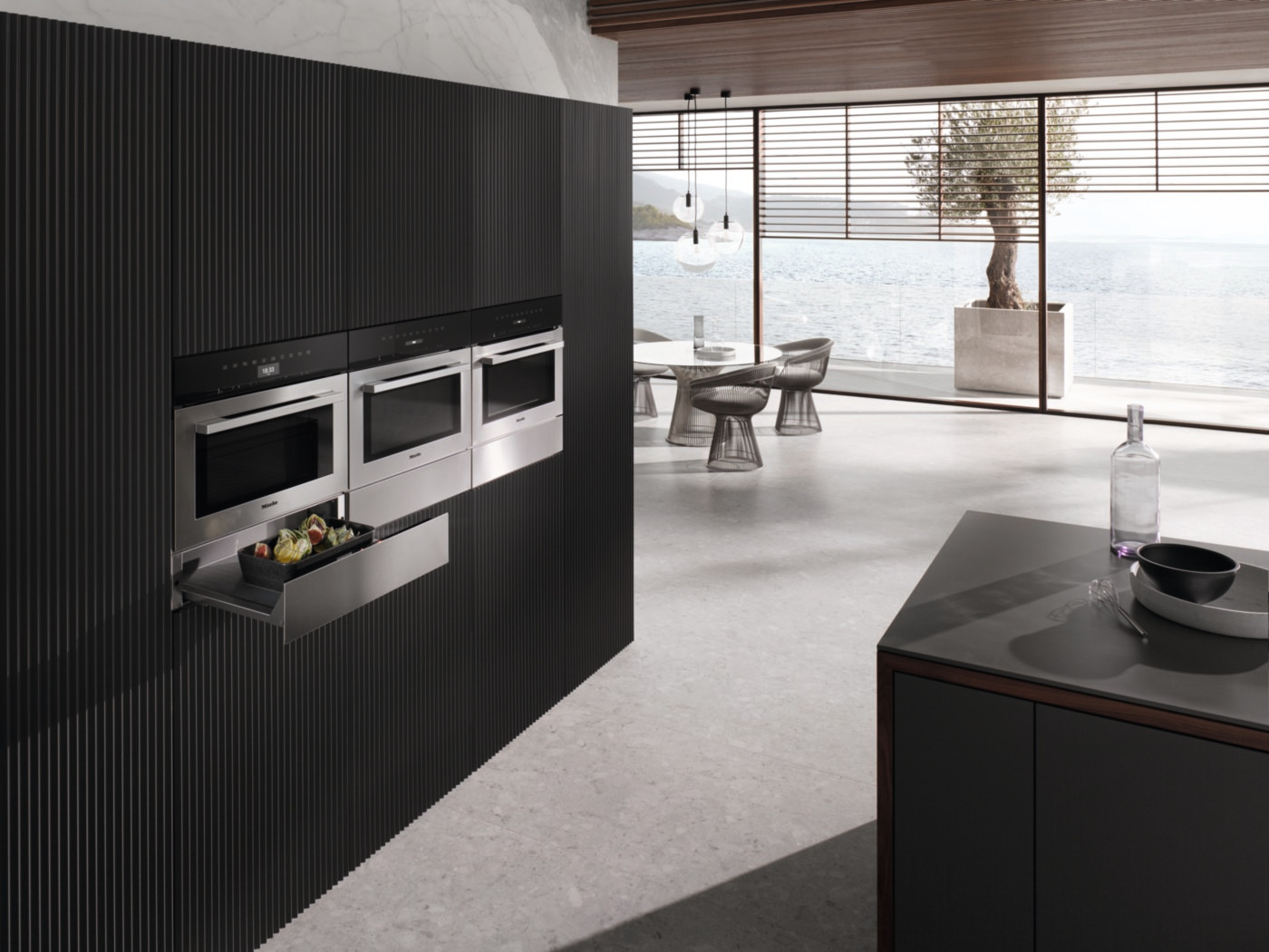 Moderne keuken met ingebouwde roestvrijstalen ovens en een lade. De muur is zwart.