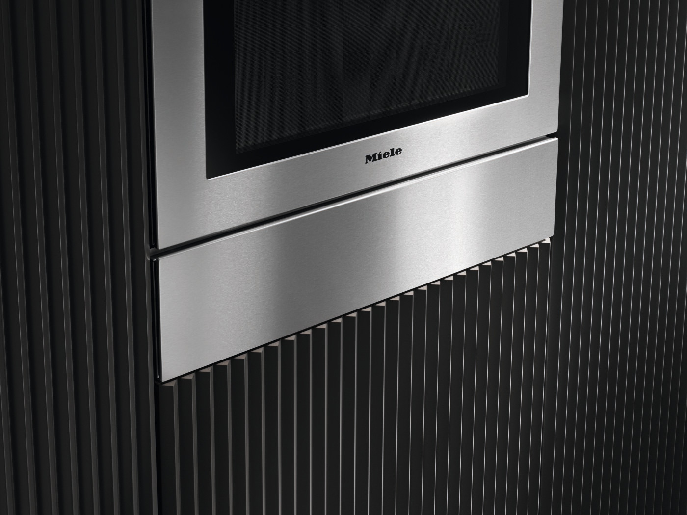 Stainless steel Miele oven with black, textured wall behind it.