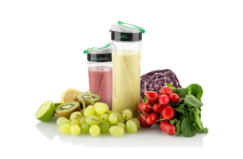 Turmixok gyümölcsökkel. Két üveg zöld és piros turmixszal, gyümölcsök fehér felületen.