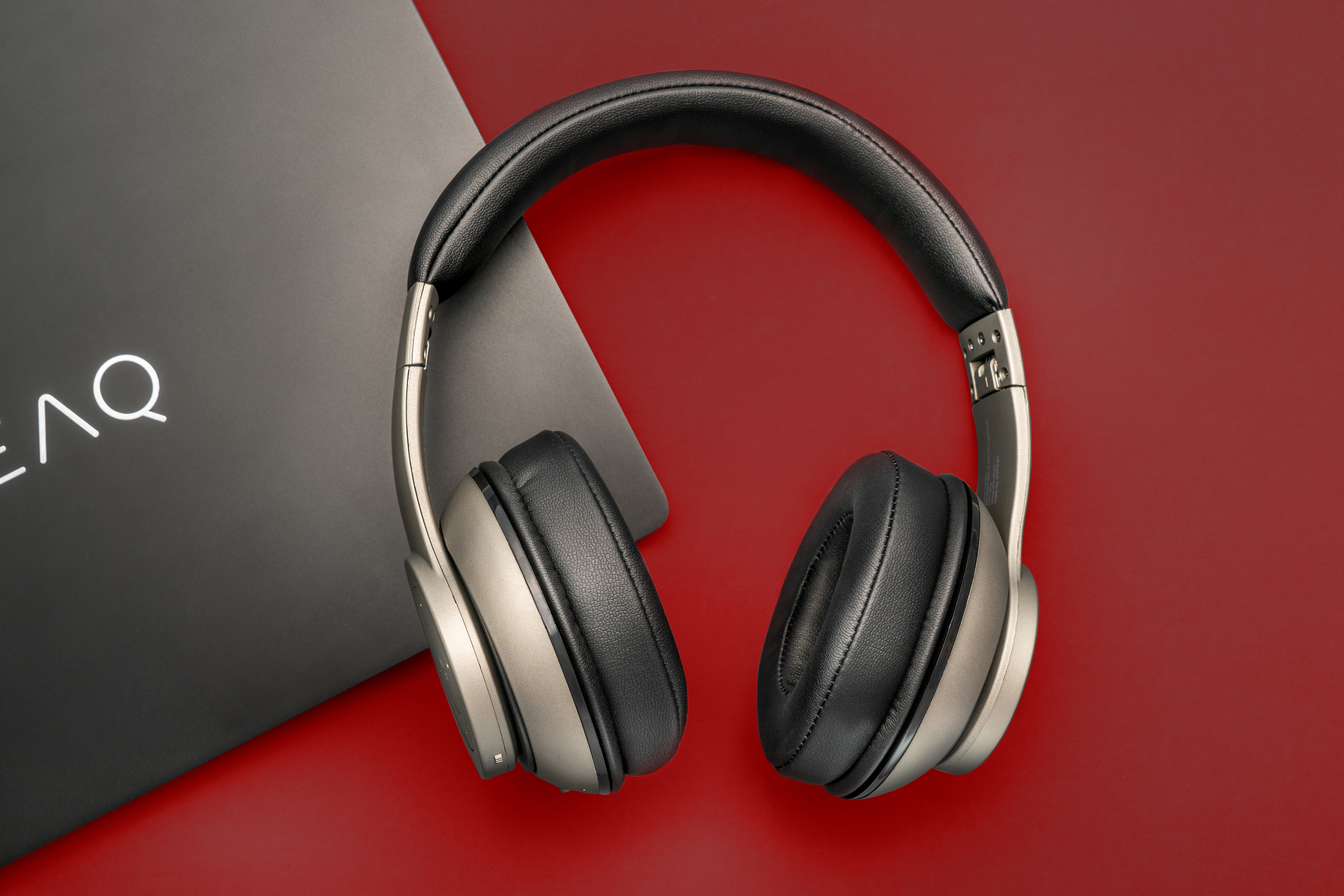 Over-Ear-Kopfhörer auf roter Oberfläche. Schwarze Ohrmuscheln und metallischer Rahmen. Ein schwarzes Quadrat im Hintergrund.