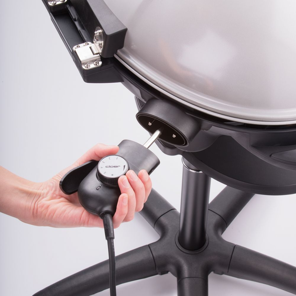 Hand stellt den Drehregler an einem schwarzen Grill ein. Grill auf schwarzem Sockel. Weißer Hintergrund.