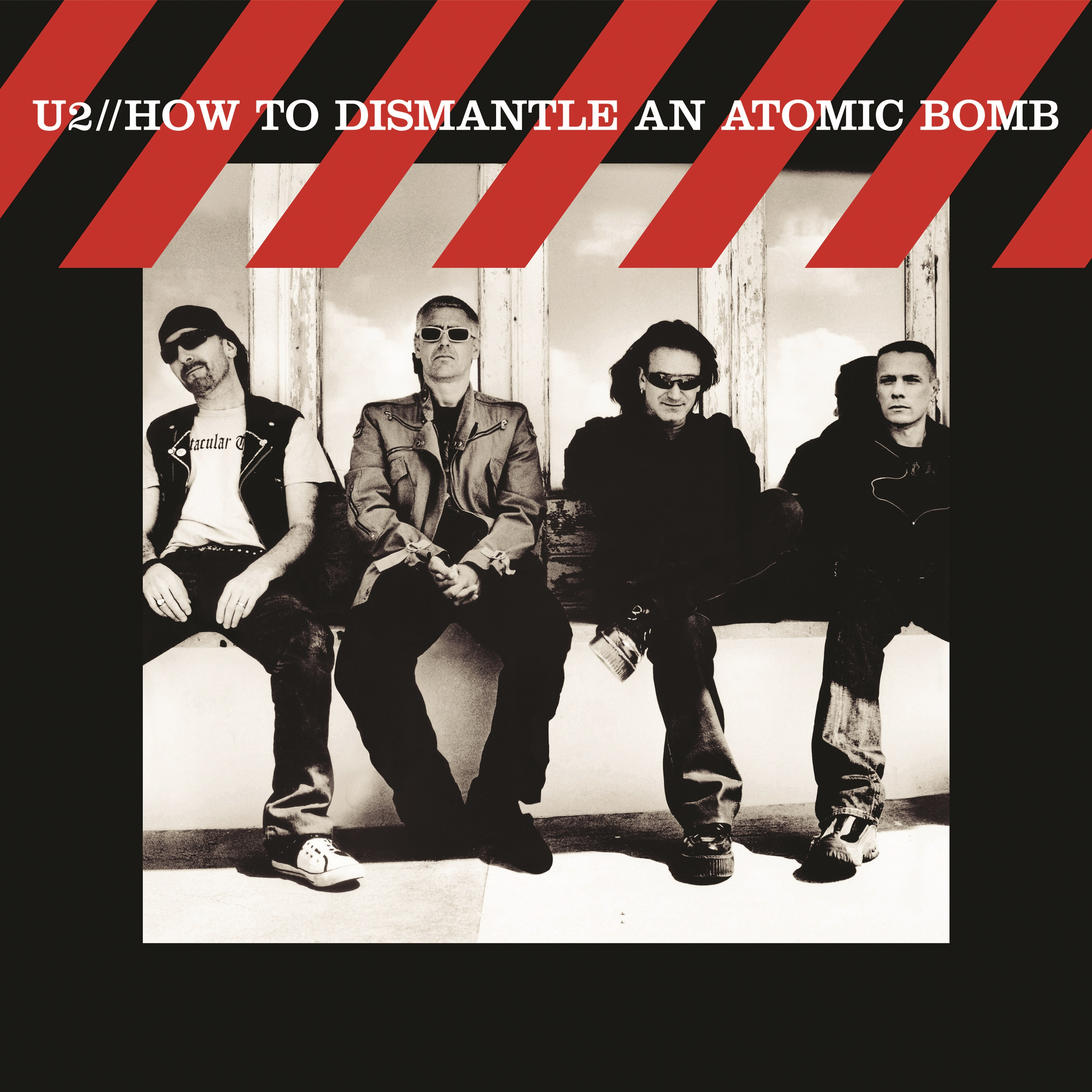 U2-Albumcover. Bandmitglieder sitzen. Rote und schwarze diagonale Streifen oben. Weißer Hintergrund.