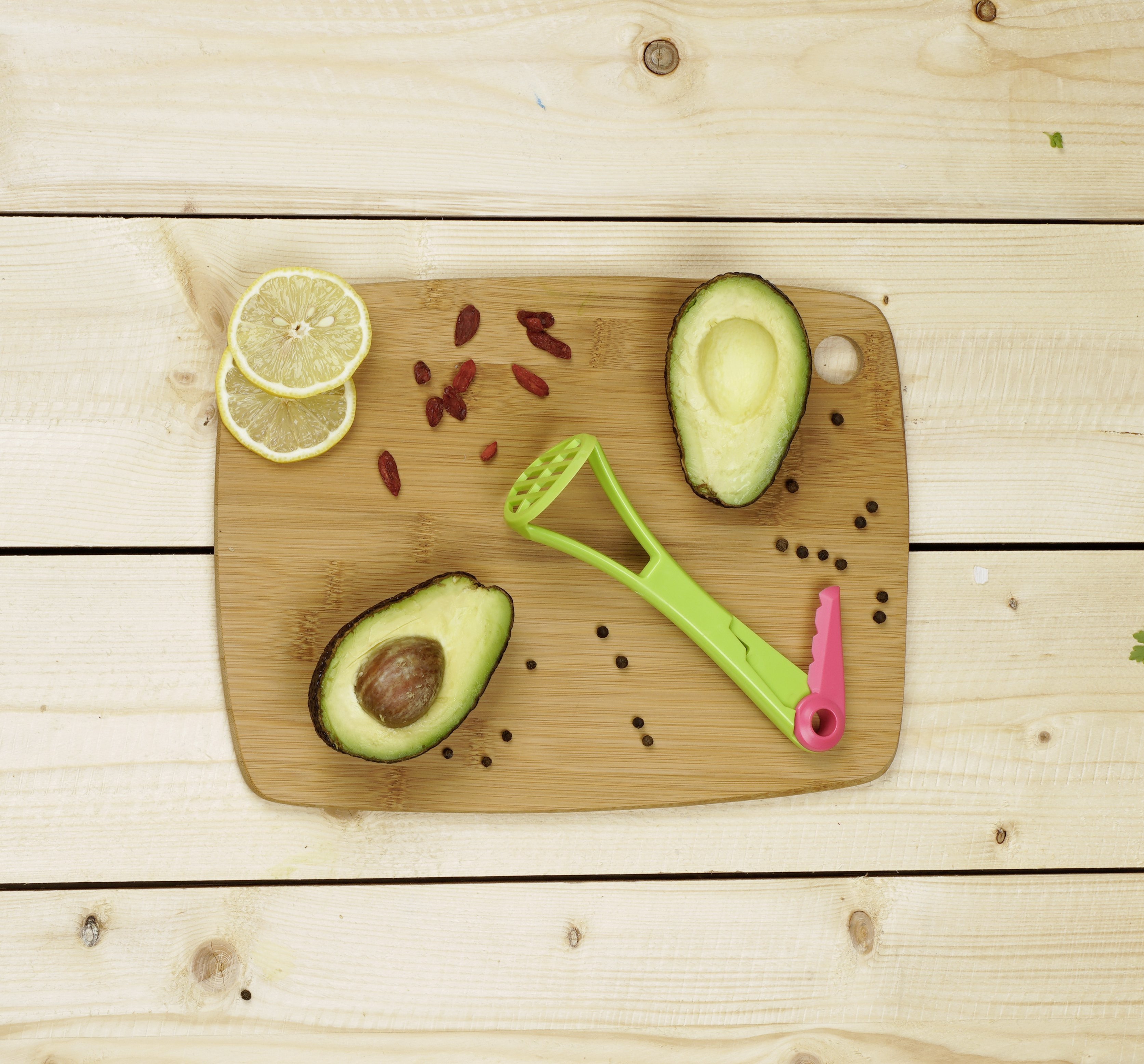 Avocadohälften, Zitronenscheiben, Goji-Beeren und grünes Werkzeug auf Brett.